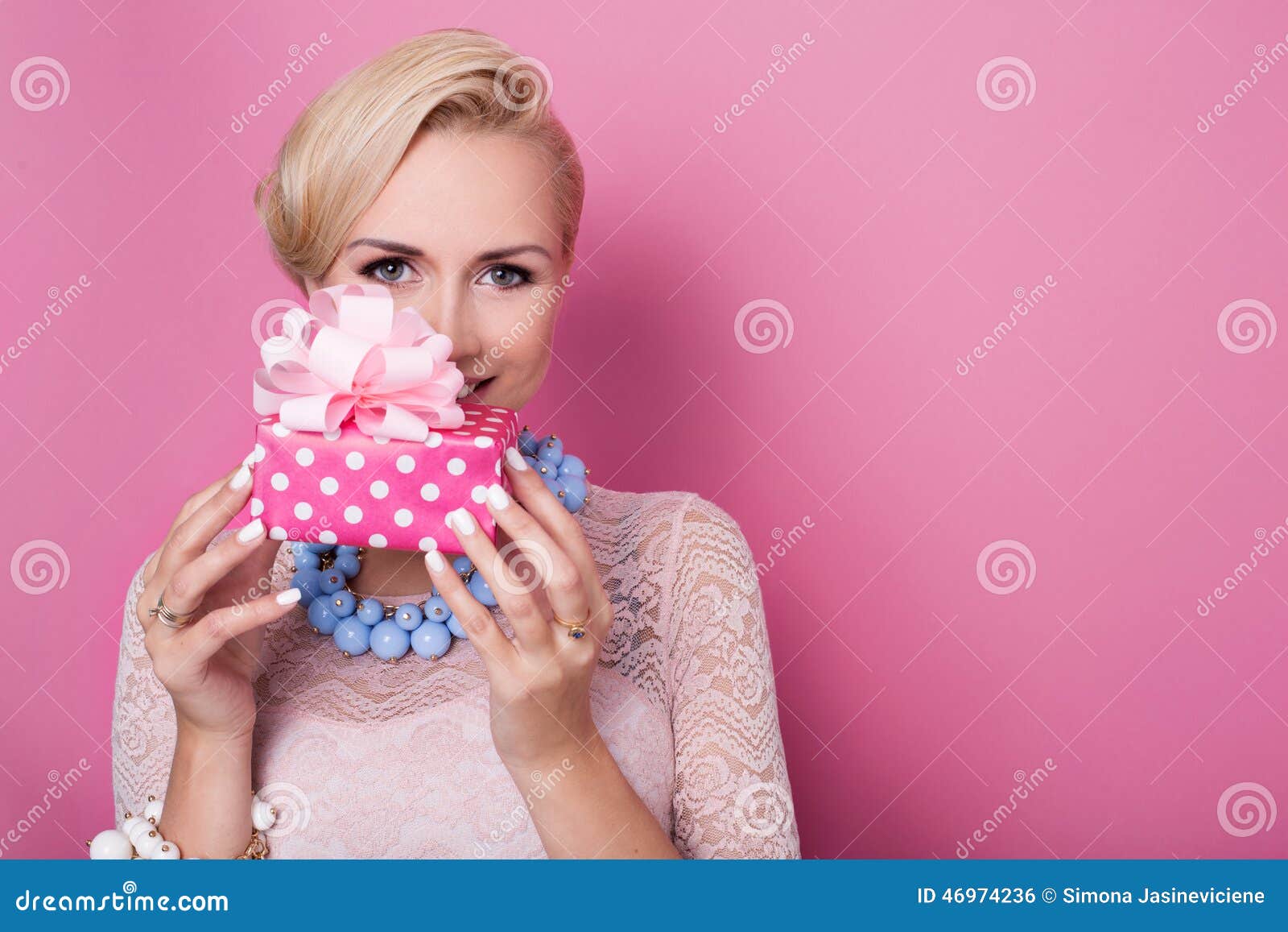 Feliz cumpleaños Mujer rubia dulce que sostiene la pequeña caja de regalo con la cinta Colores suaves Retrato del estudio sobre fondo rosado