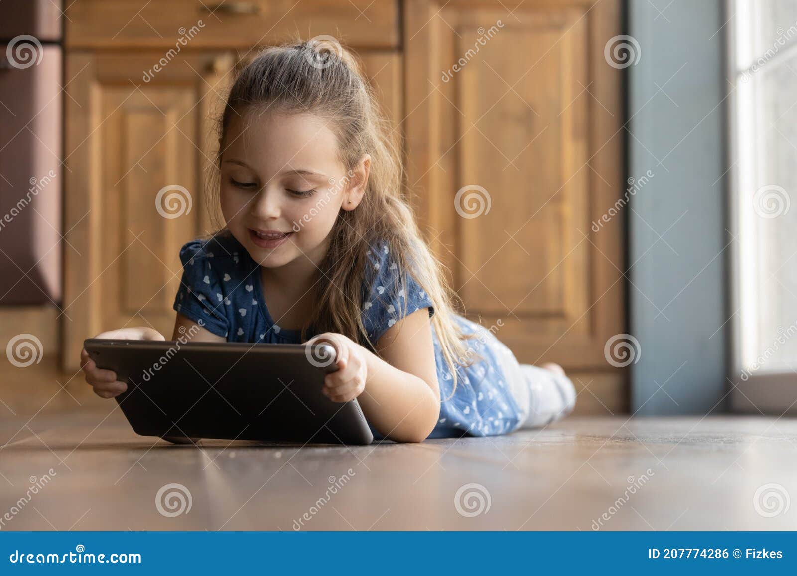 menina bonitinha sentada no chão usando tablet digital tocando a