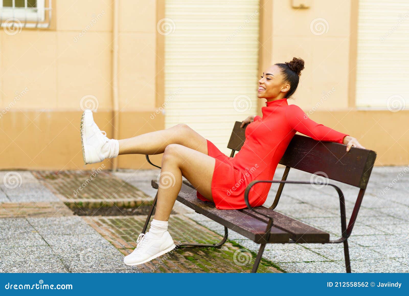 Feliz Mujer Mixta Moviendo Las Piernas En Alegría Sentada En Un Banco En La  Calle. Foto de archivo - Imagen de rizado, mezclado: 212558562