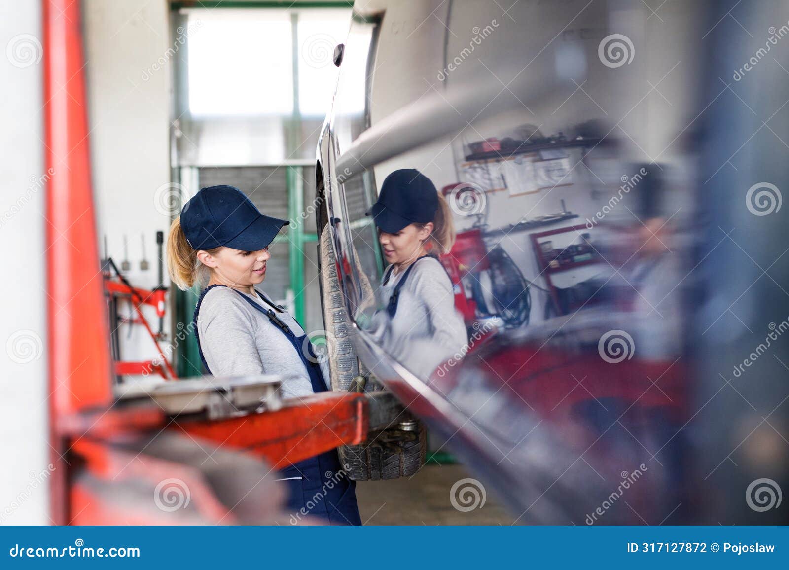 female auto mechanic changing tieres in auto service. beautiful woman holding tire in a garage, wearing blue coveralls.