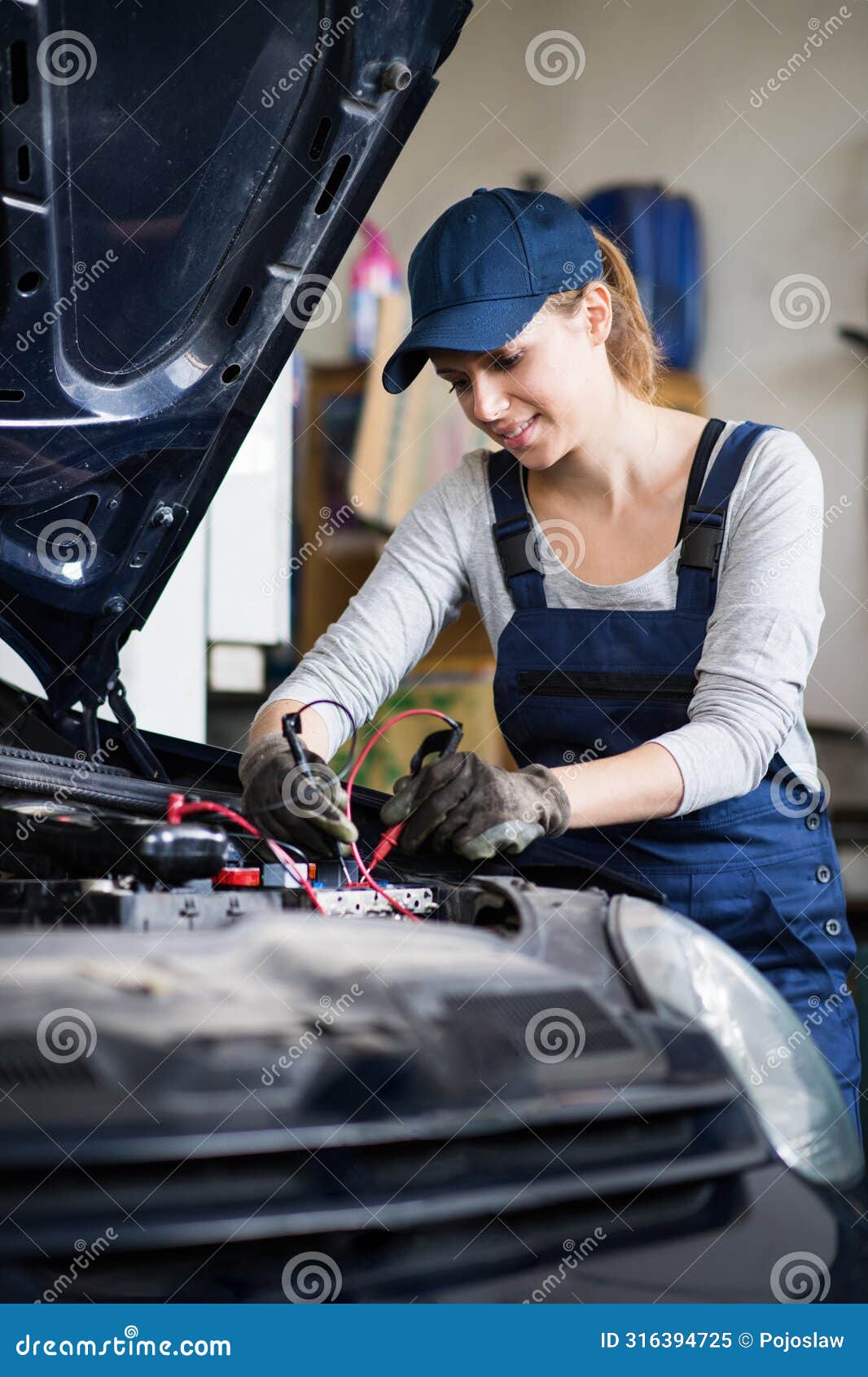 female auto mechanic repairing, maintaining car, car battery. beautiful woman working in a garage, wearing blue