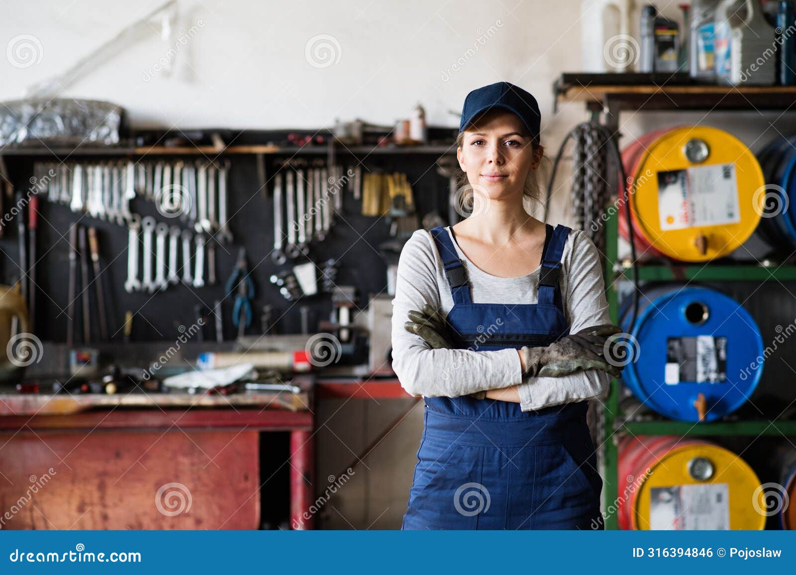female auto mechanic repairing, maintaining car. beautiful woman standing in a garage, wearing blue coveralls.