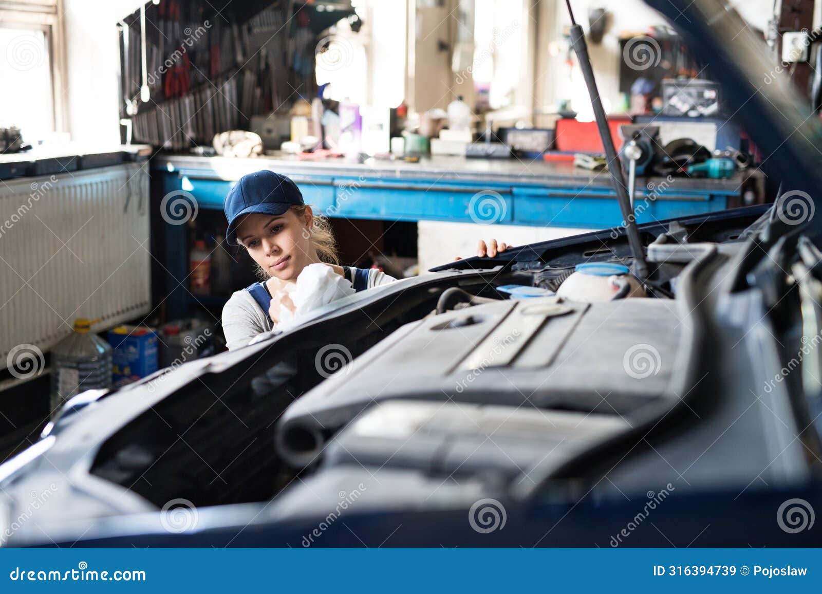 female auto mechanic repairing, maintaining car. beautiful woman working in a garage, wearing blue coveralls.