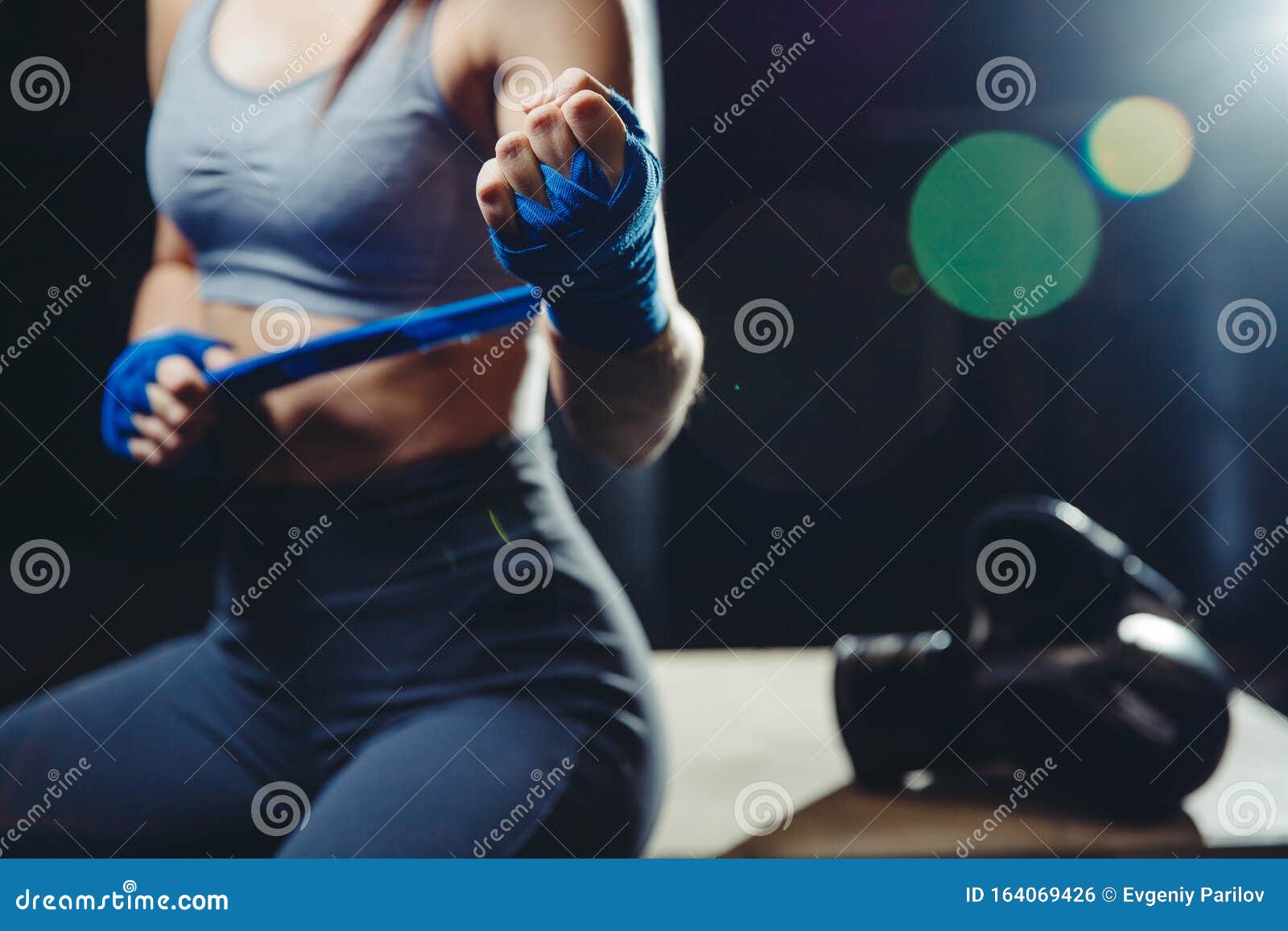 female boxer pulls white bandage strap around her wrist in blue. concept femenism, independence