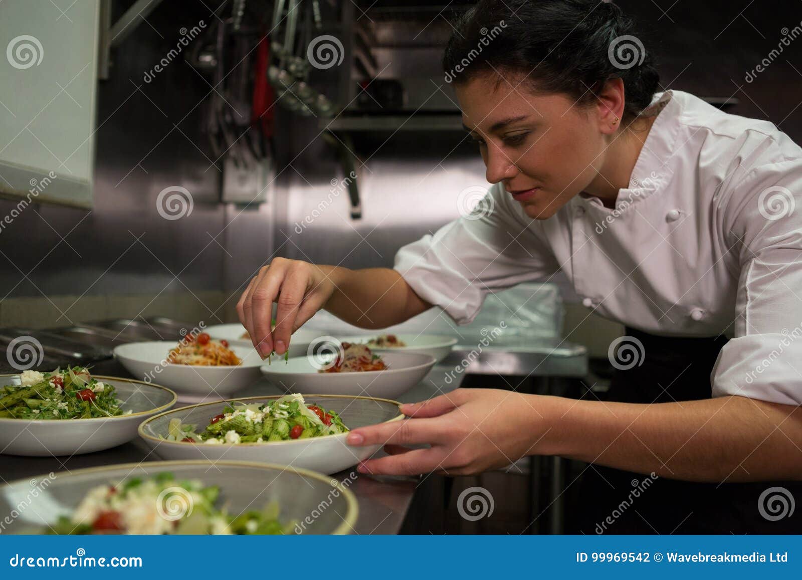 female chef garnishing appetizer plates at order station