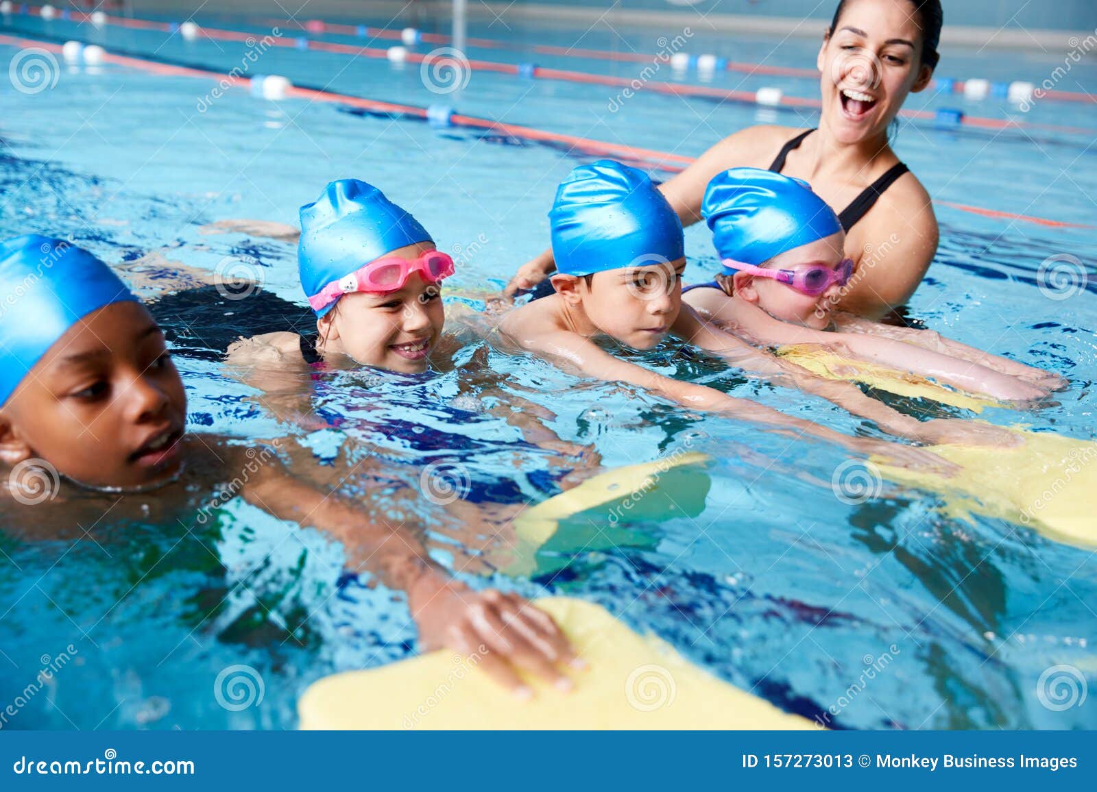 female coach in water giving group of children swimming lesson in indoor pool