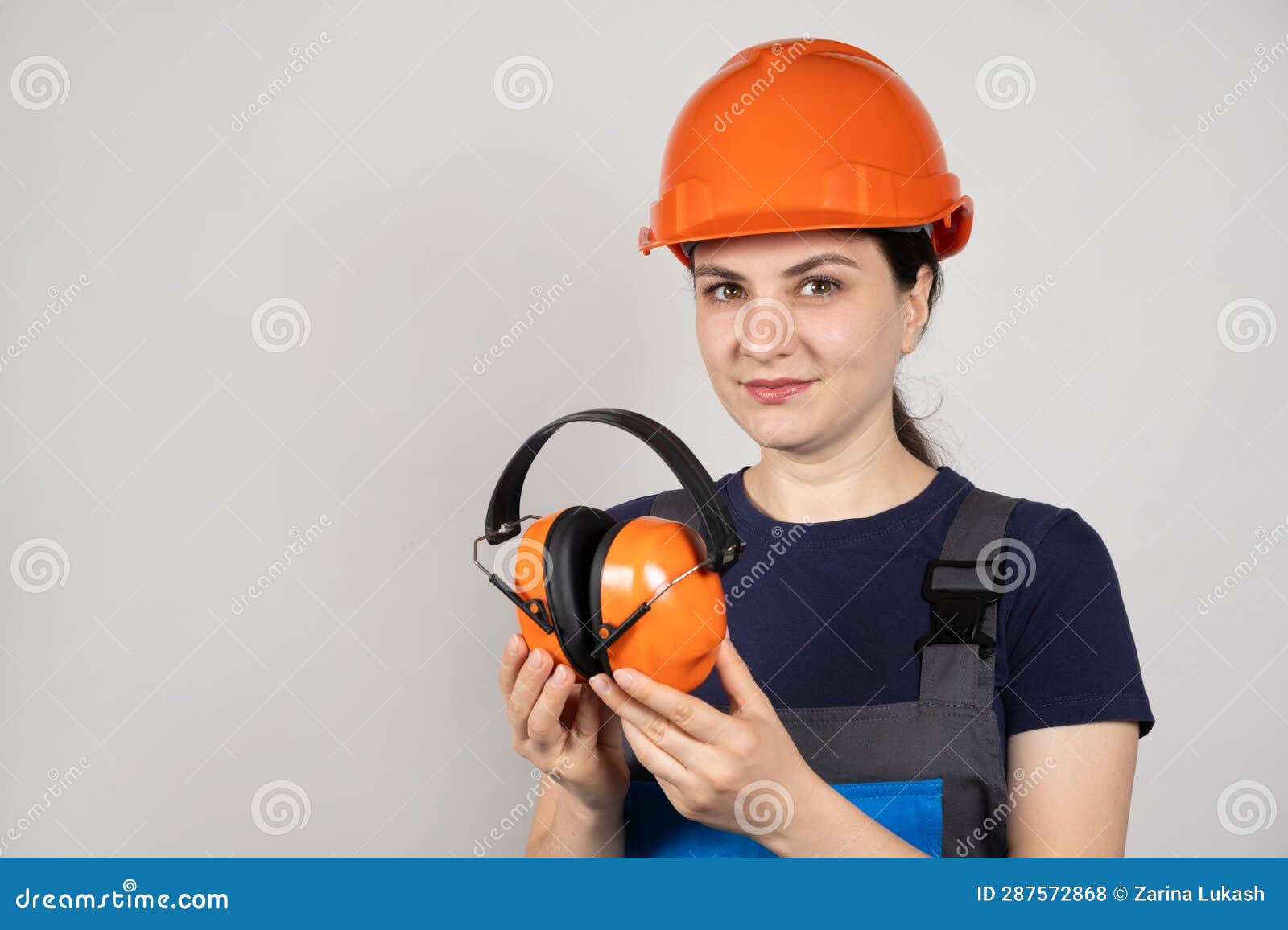 Female Construction Worker in Protective Helmet Holding Earmuffs on