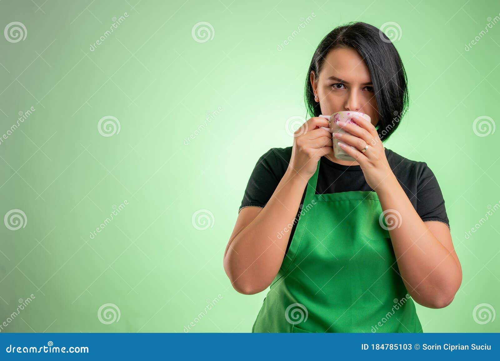 female cook with green apron and black t-shirt drinking cafee