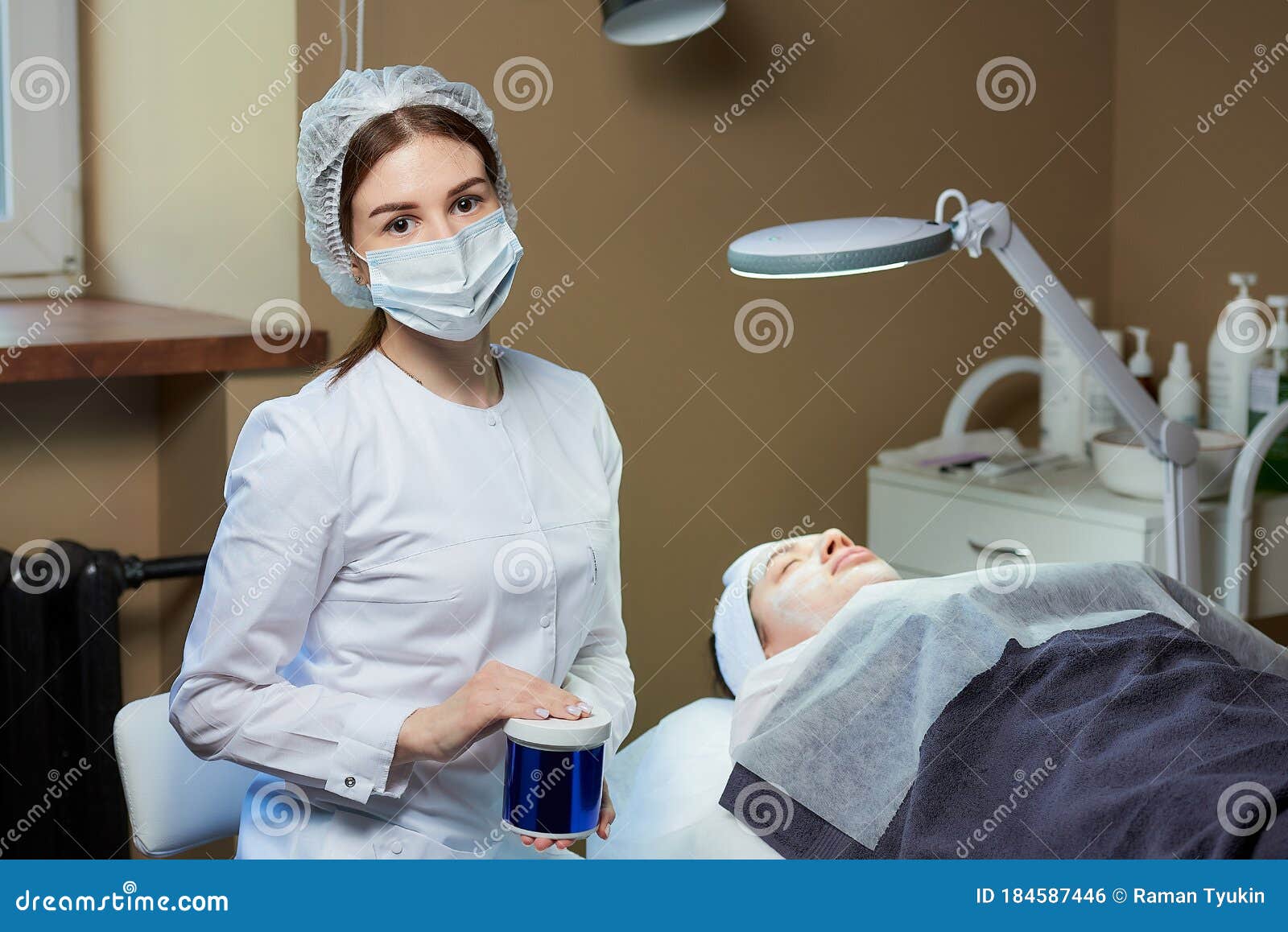 A Female Cosmetologist In A Mask Posing With A Skincare Product Near A