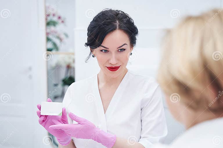 Female Cosmetologist Showing Cosmetic Cream To Client In Spa Salon