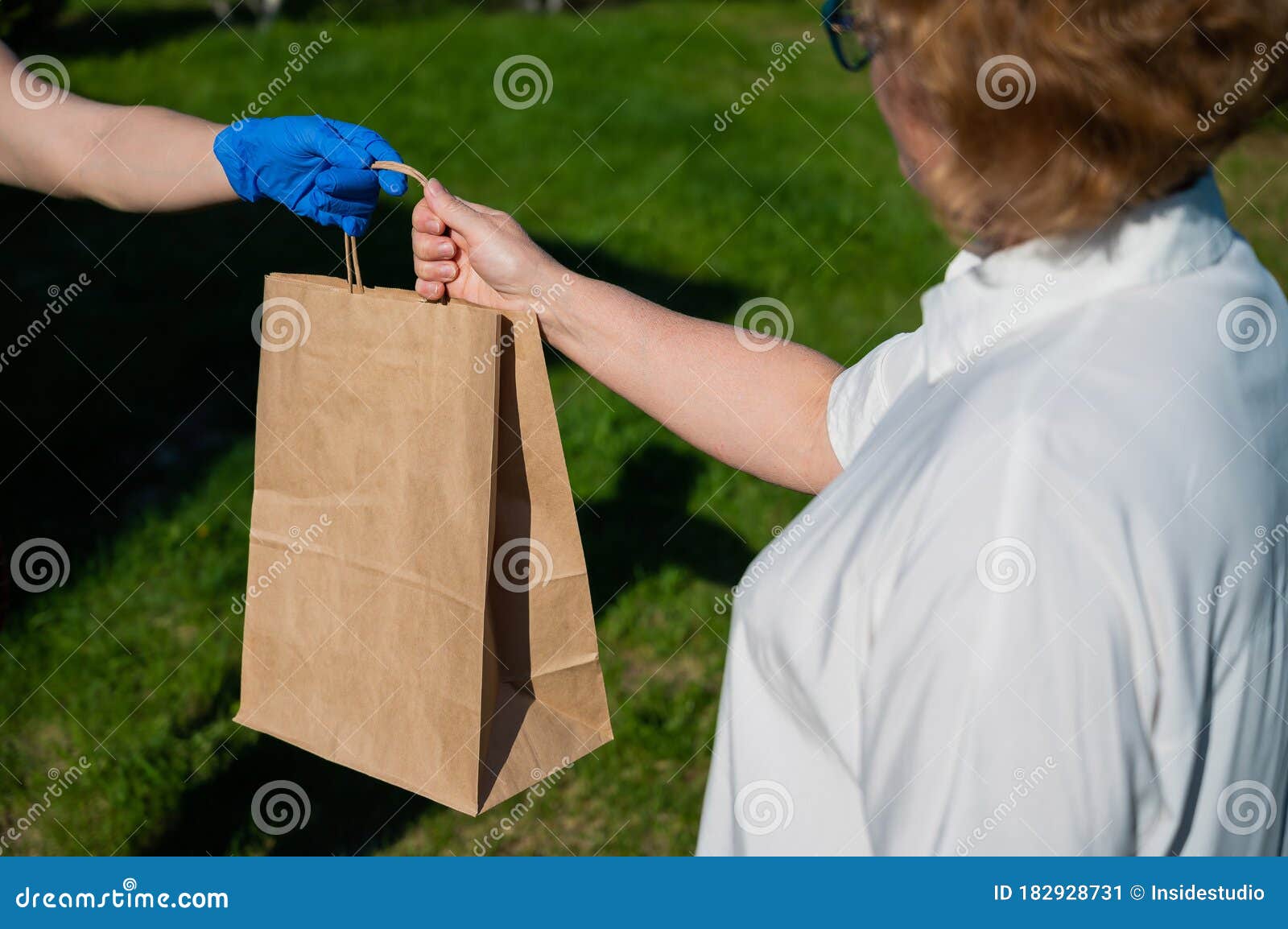 female courier in gloves bringing food package to retired old woman. woman handing a paper bag with groceries to a