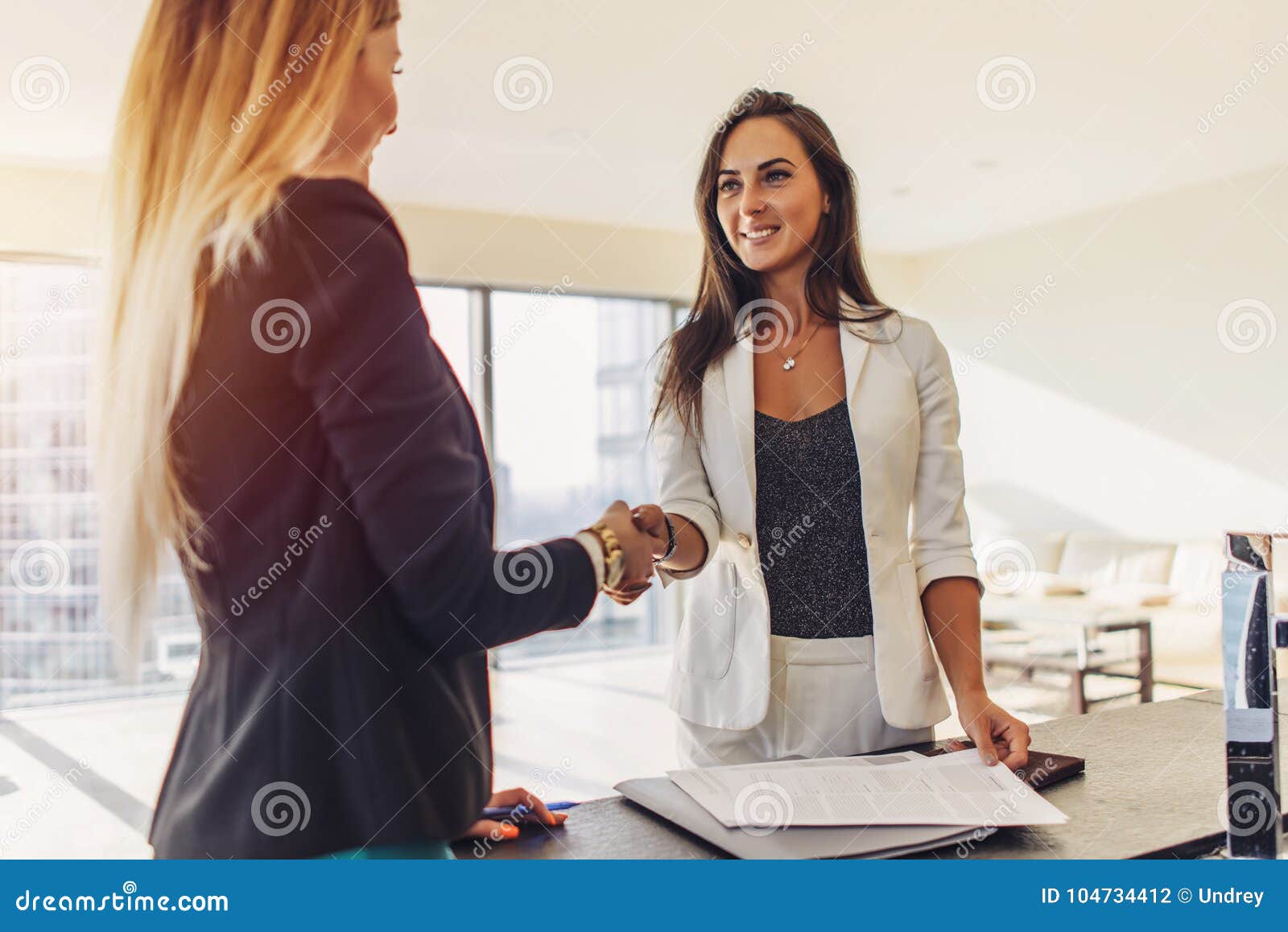 female customer shaking hands with real estate agent agreeing to sign a contract standing in new modern studio apartment