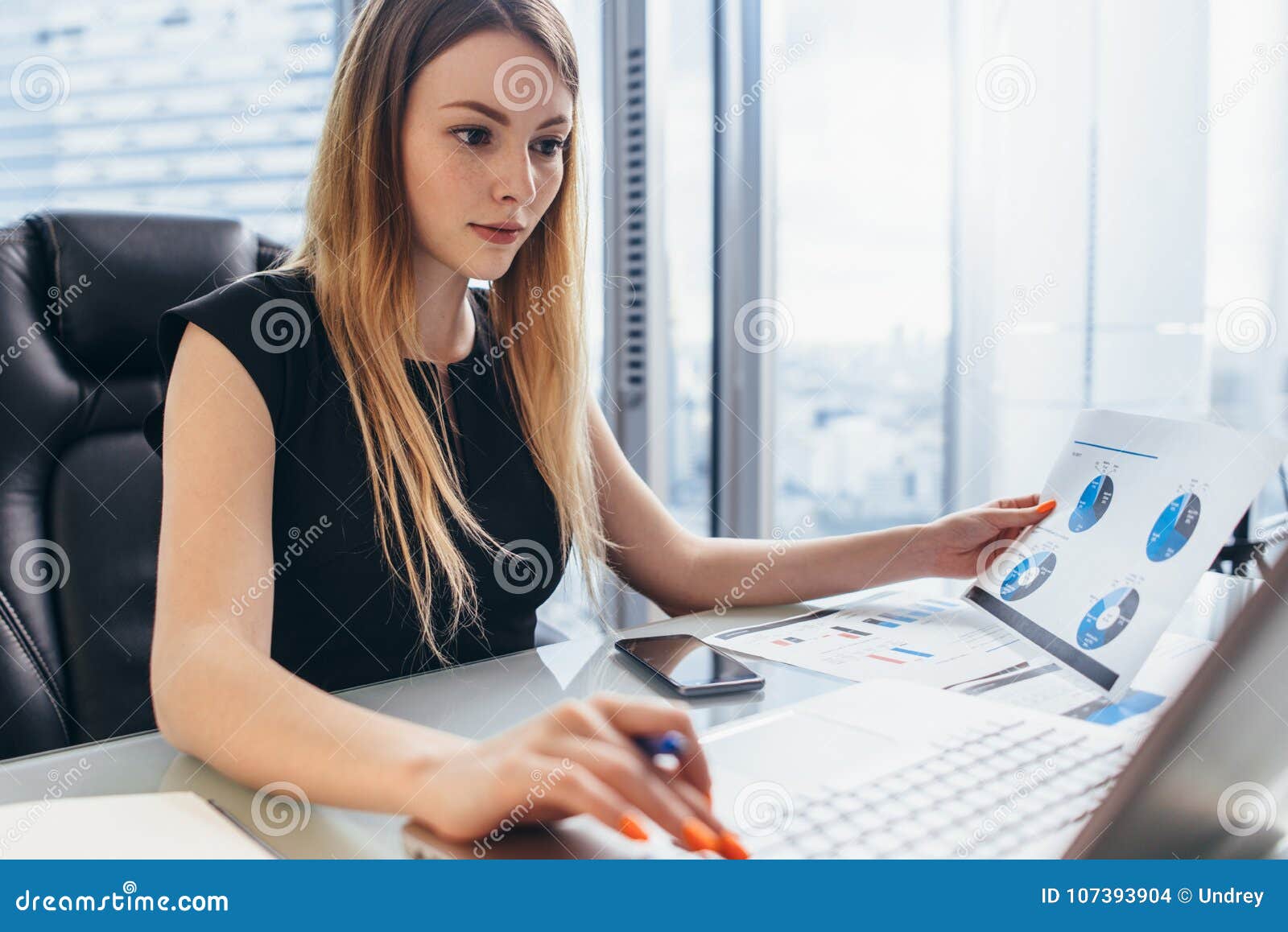 female director working in office sitting at desk analyzing business statistics holding diagrams and charts using laptop