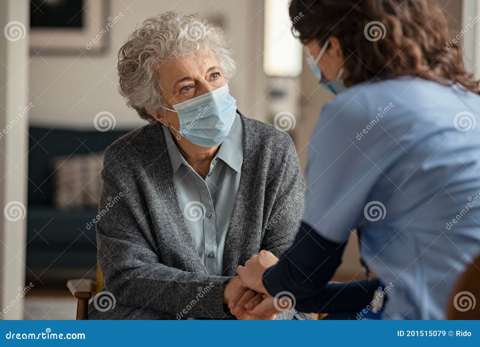 female doctor consoling senior woman wearing face mask during home visit