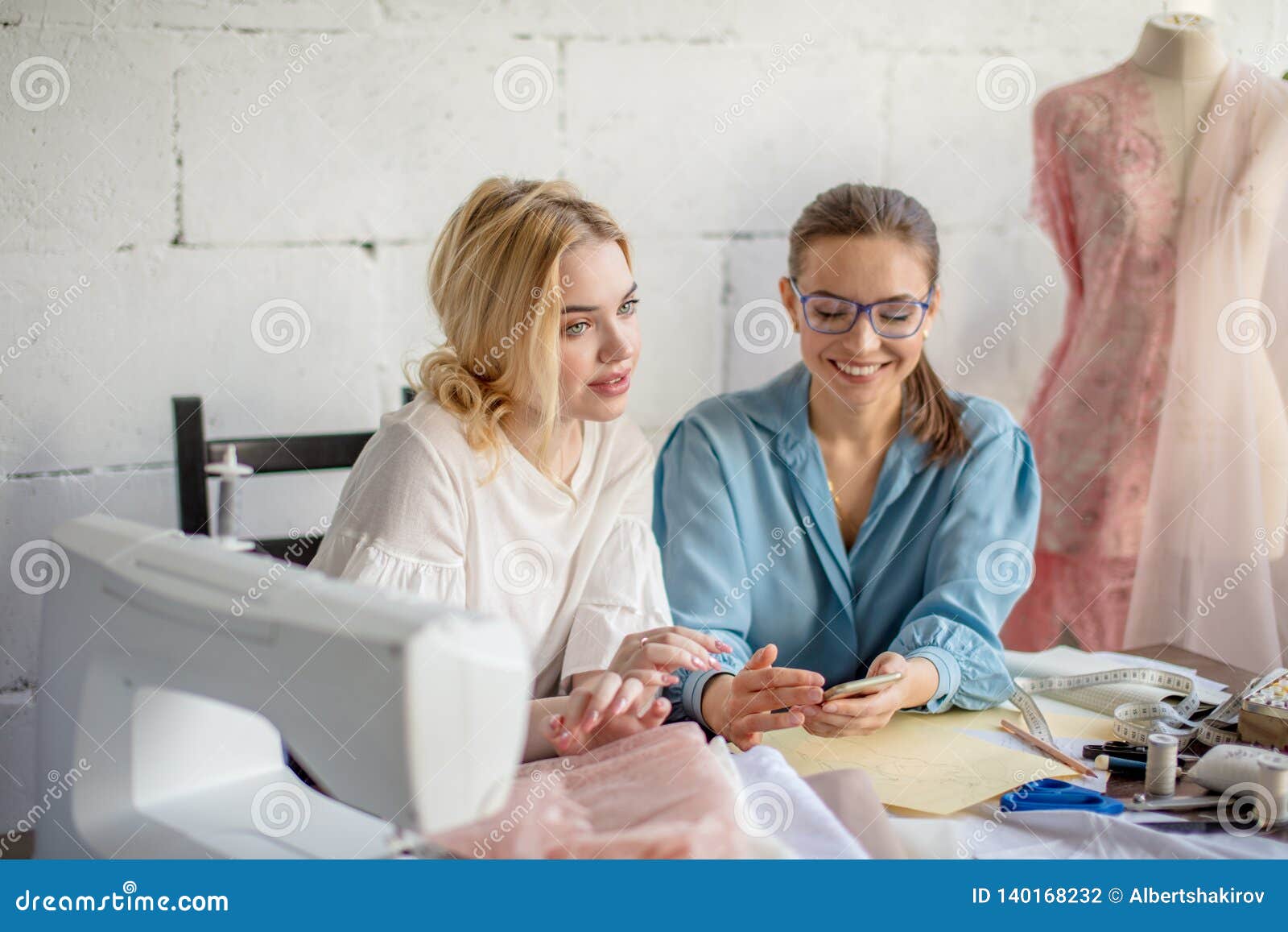 Female Dressmaker Showing Design To Her Client, Sitting Together at ...