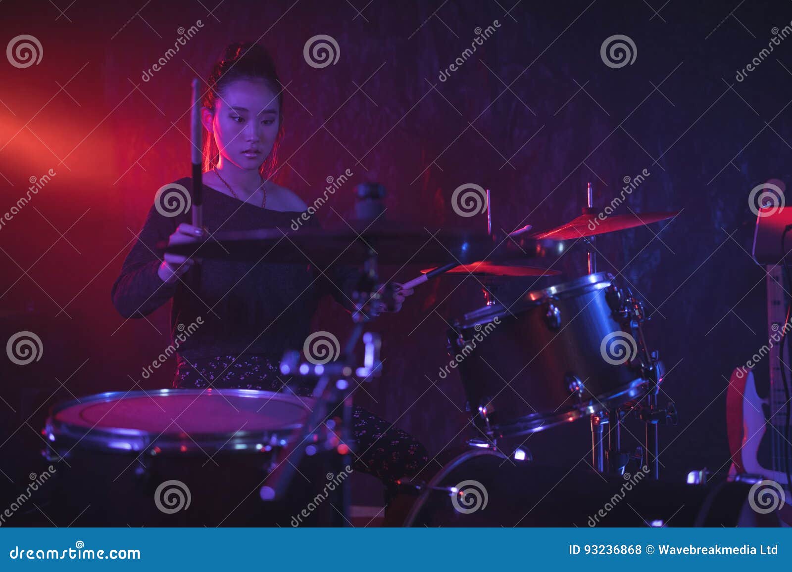 Female Drummer Playing Drum Kit in Illuminated Stock Photo