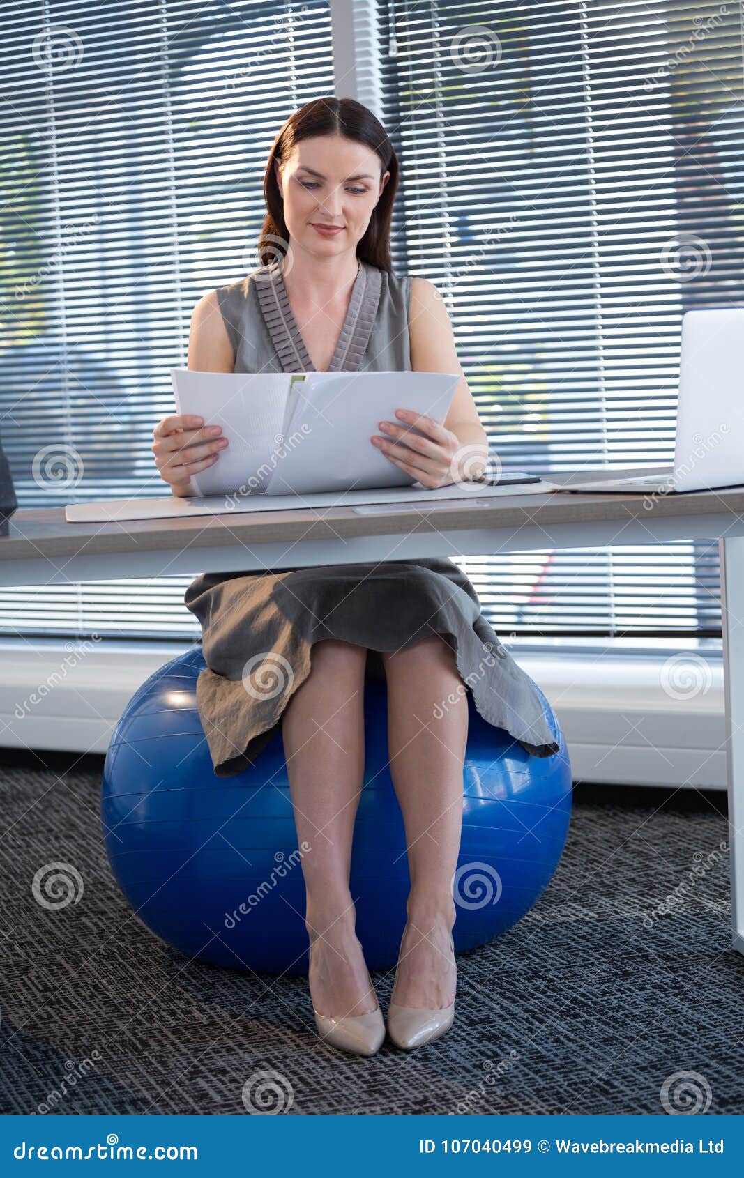 Female Executive Sitting On Exercise Ball While Reading Documents