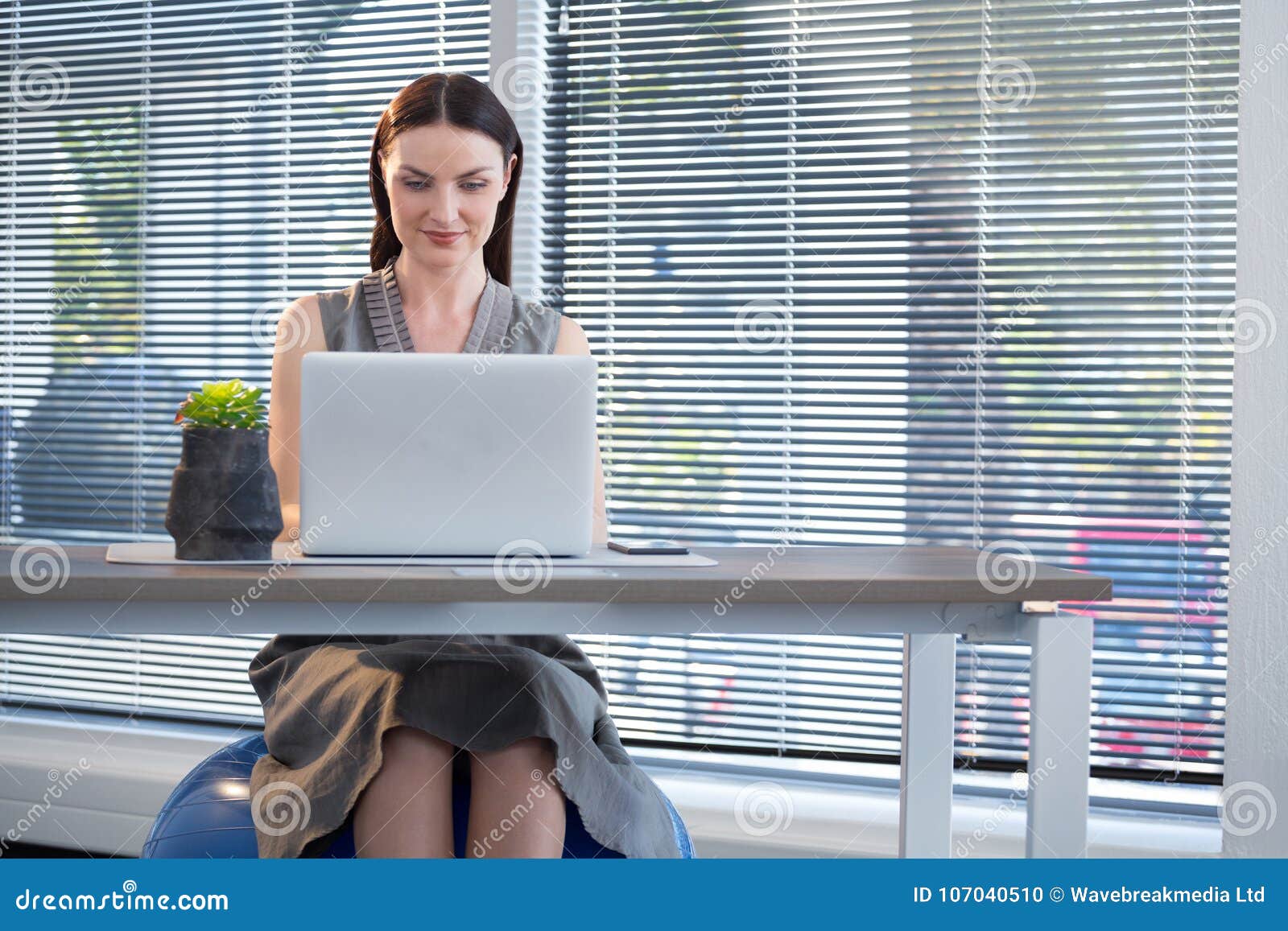 Female Executive Sitting On Exercise Ball While Working At Desk