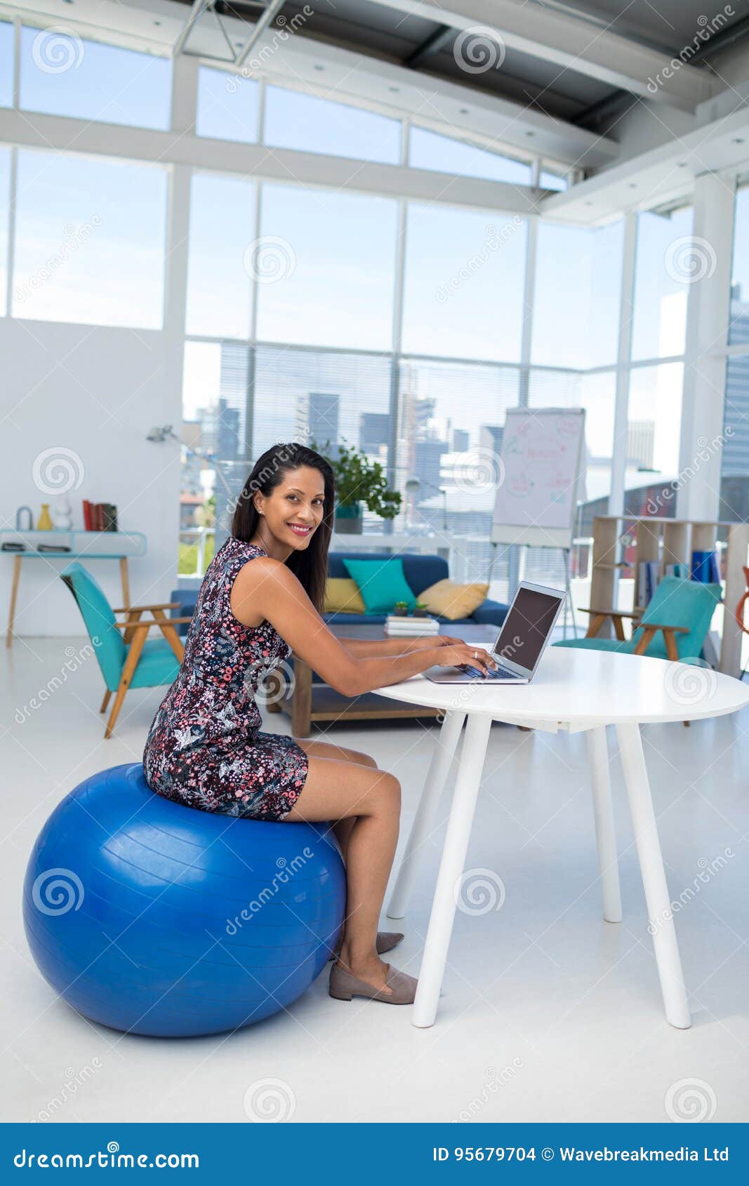 Female Executive Using Laptop While Sitting On Exercise Ball At