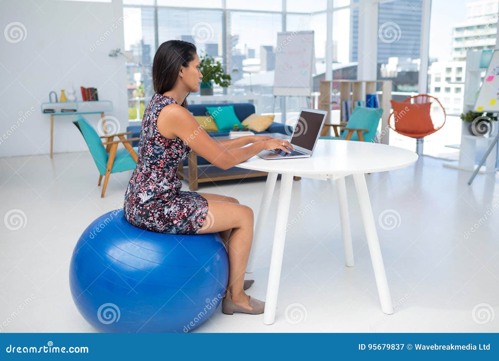 Female Executive Using Laptop While Sitting On Exercise Ball At