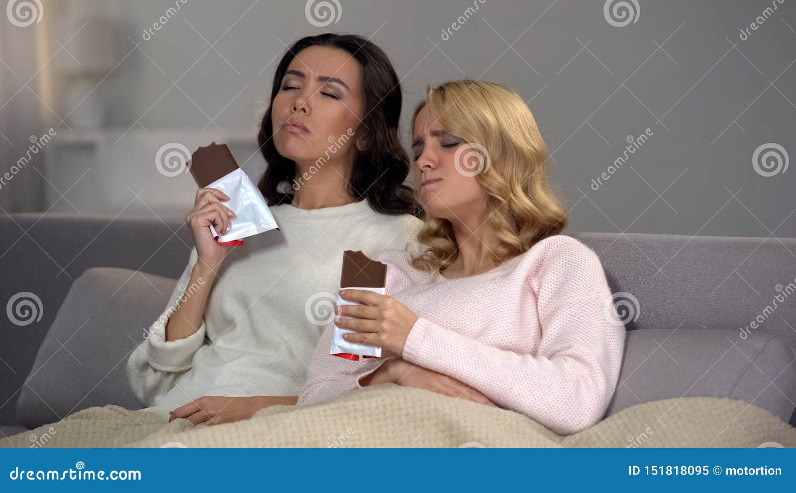 female friends sitting on sofa and enjoying sweet chocolate taste, hormones