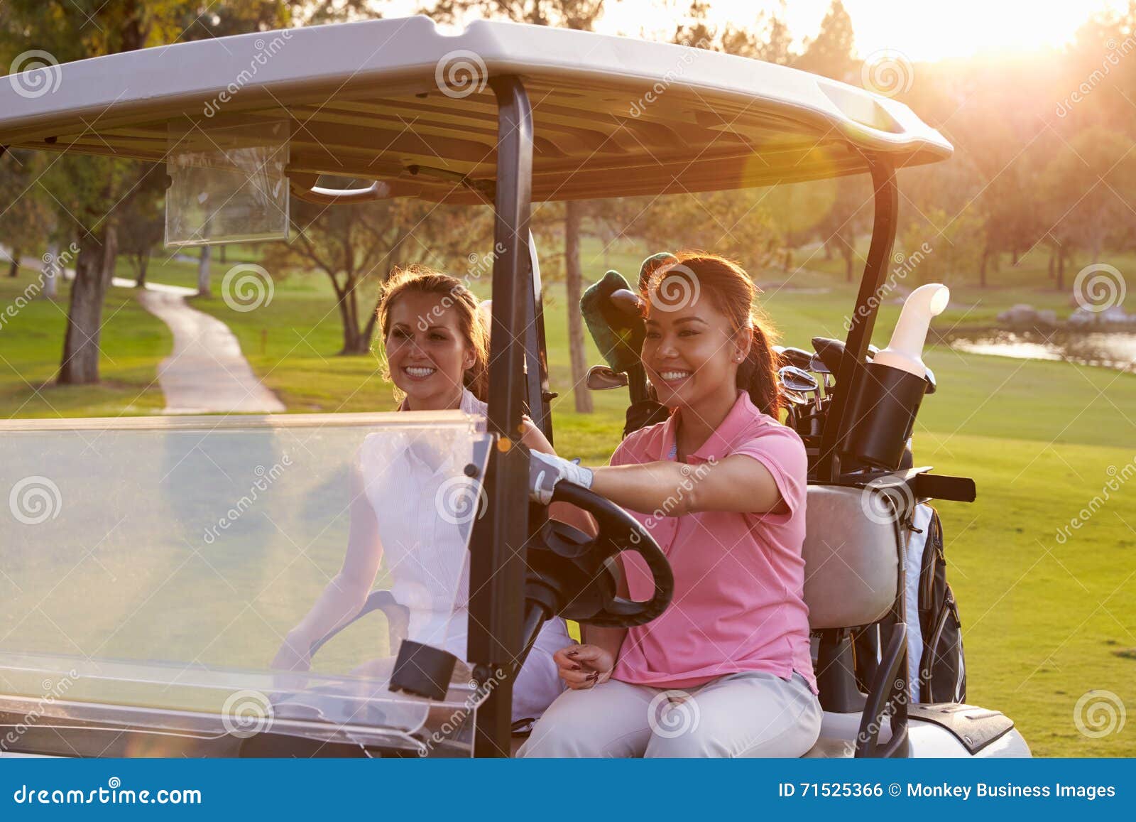 Female Golfers Driving Buggy Along Fairway of Golf Course Stock Photo