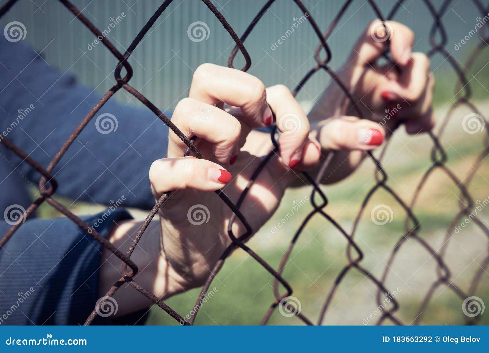 female hands grabbed the metal mesh of the fence, concept
