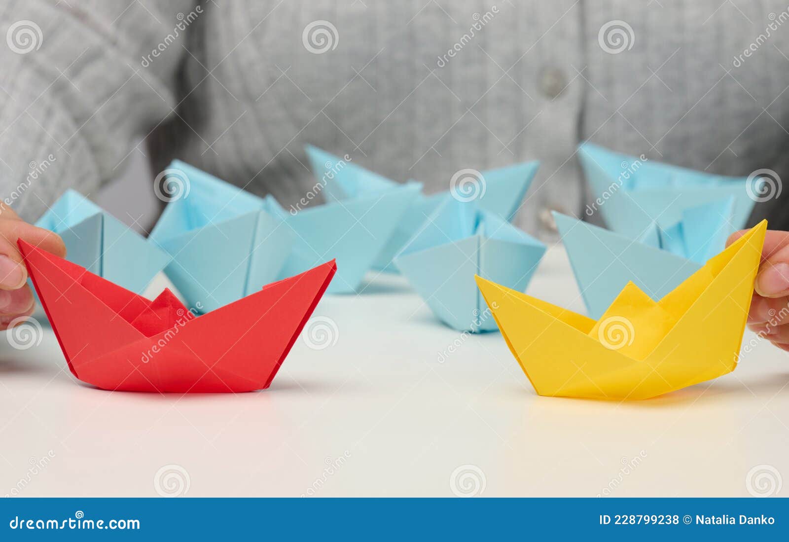 female hands hold red and yellow paper boats on a white table. confrontation, follow a strong leader, dailog
