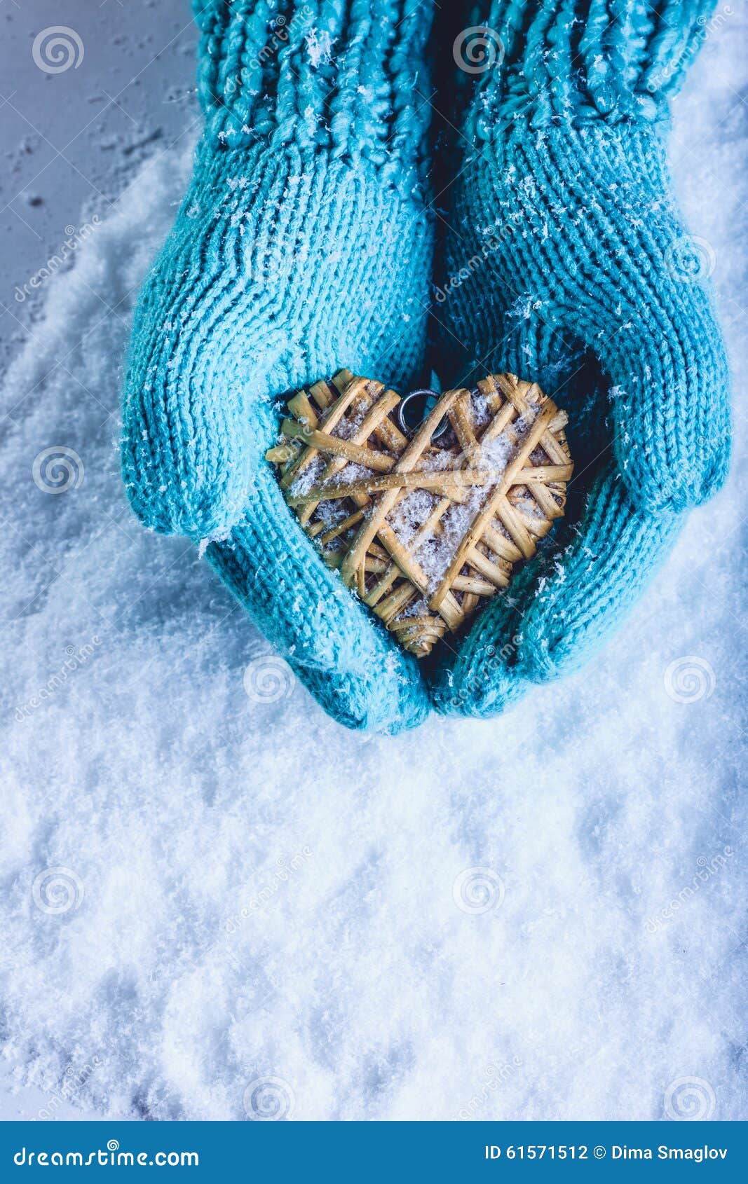female hands in light teal knitted mittens with entwined beige flaxen heart on a white snow background. st. valentines day concept