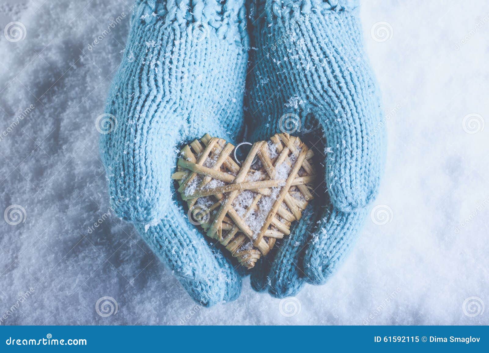 female hands in light teal knitted mittens with entwined beige flaxen heart on a white snow. love, st. valentines day concept