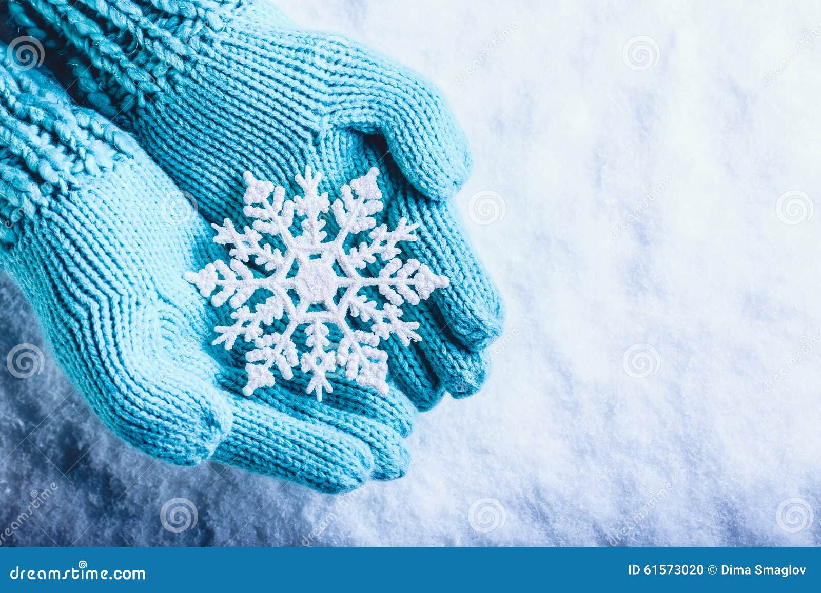 female hands in light teal knitted mittens with sparkling wonderful snowflake on a white snow background. winter christmas concept