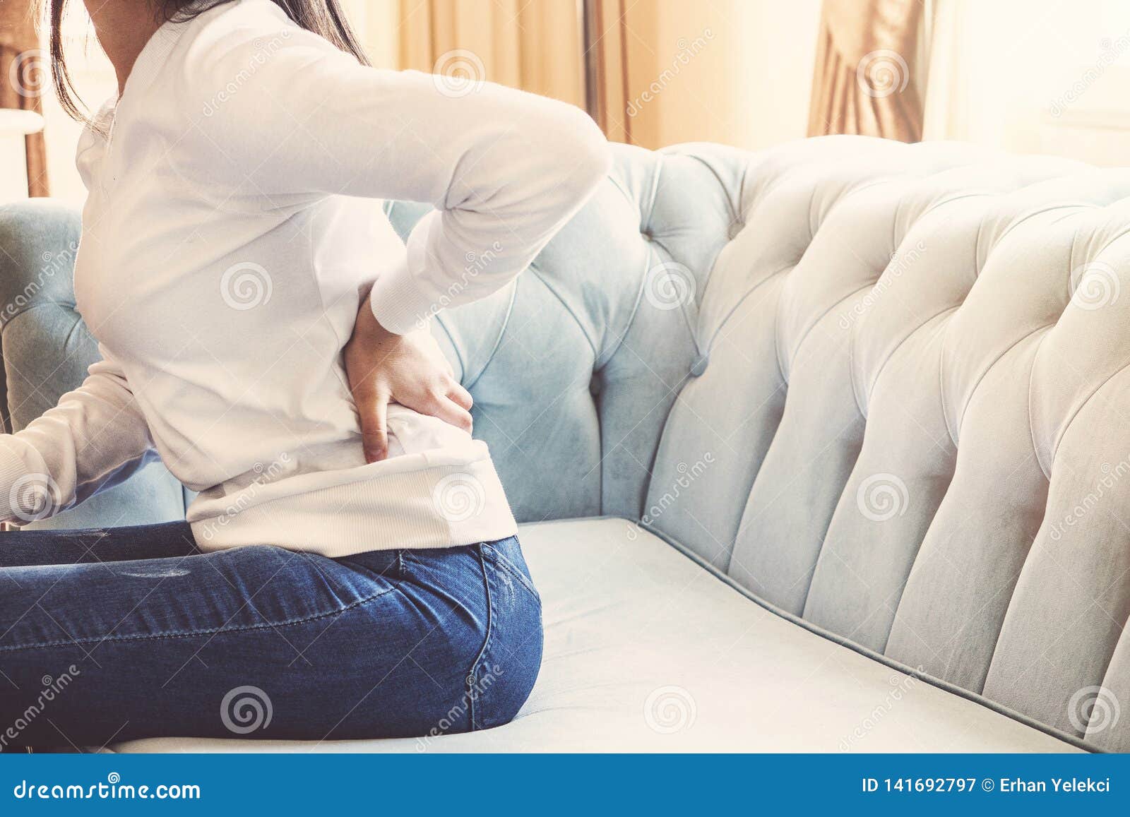 female hands touching back pain sitting in sofa resting at home. young woman low waist hurt massage.
