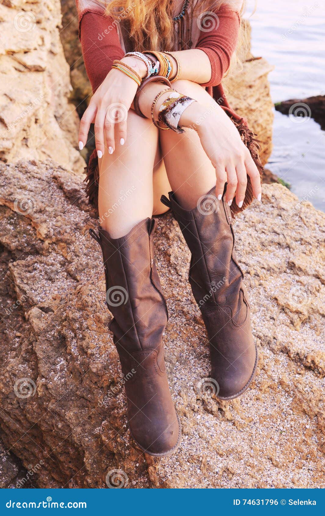 female hands with white manicure and boho chic bracelets and legs dressed in leather boots