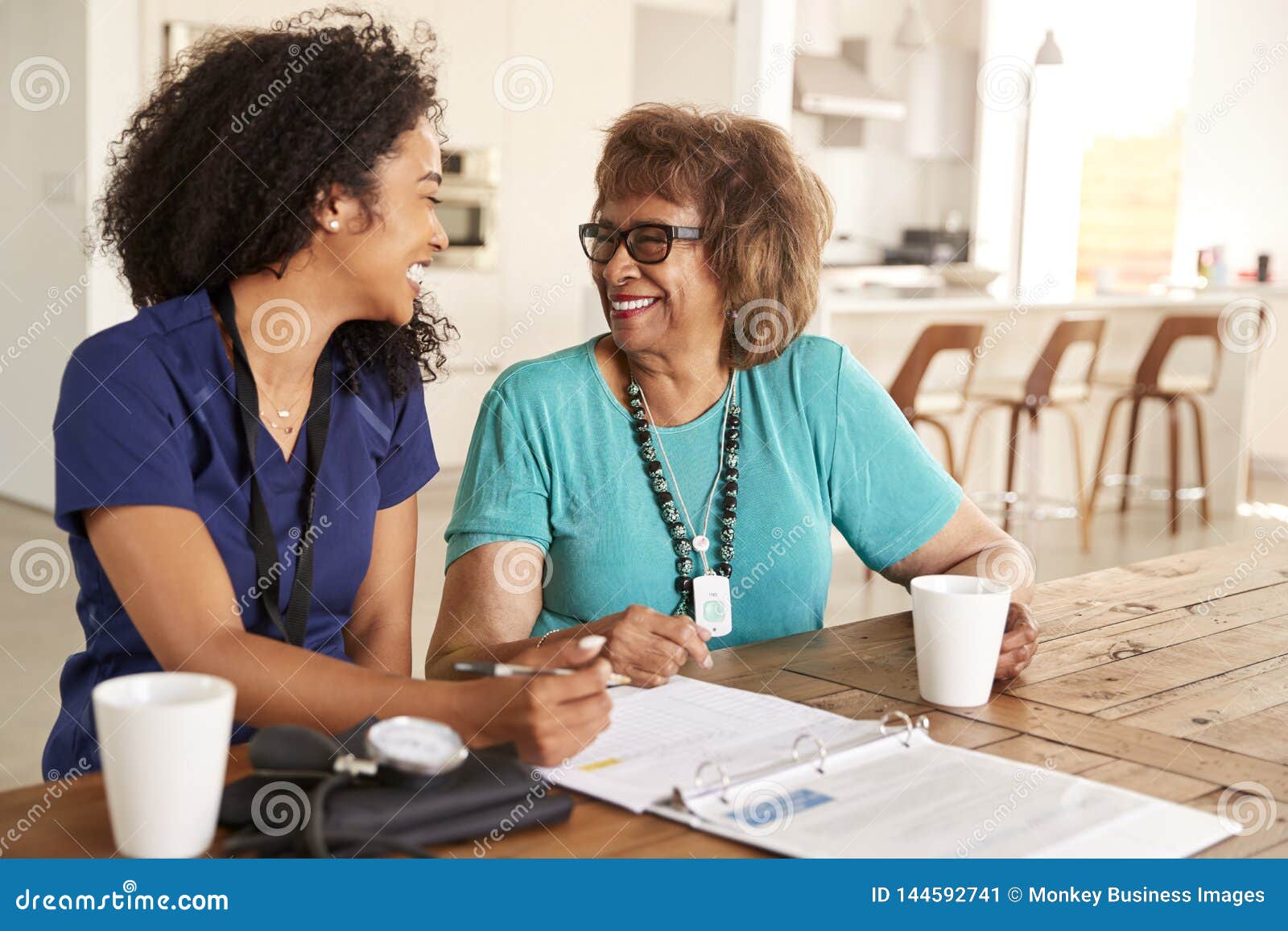 female healthcare worker sitting at table smiling with a senior woman during a home health visit