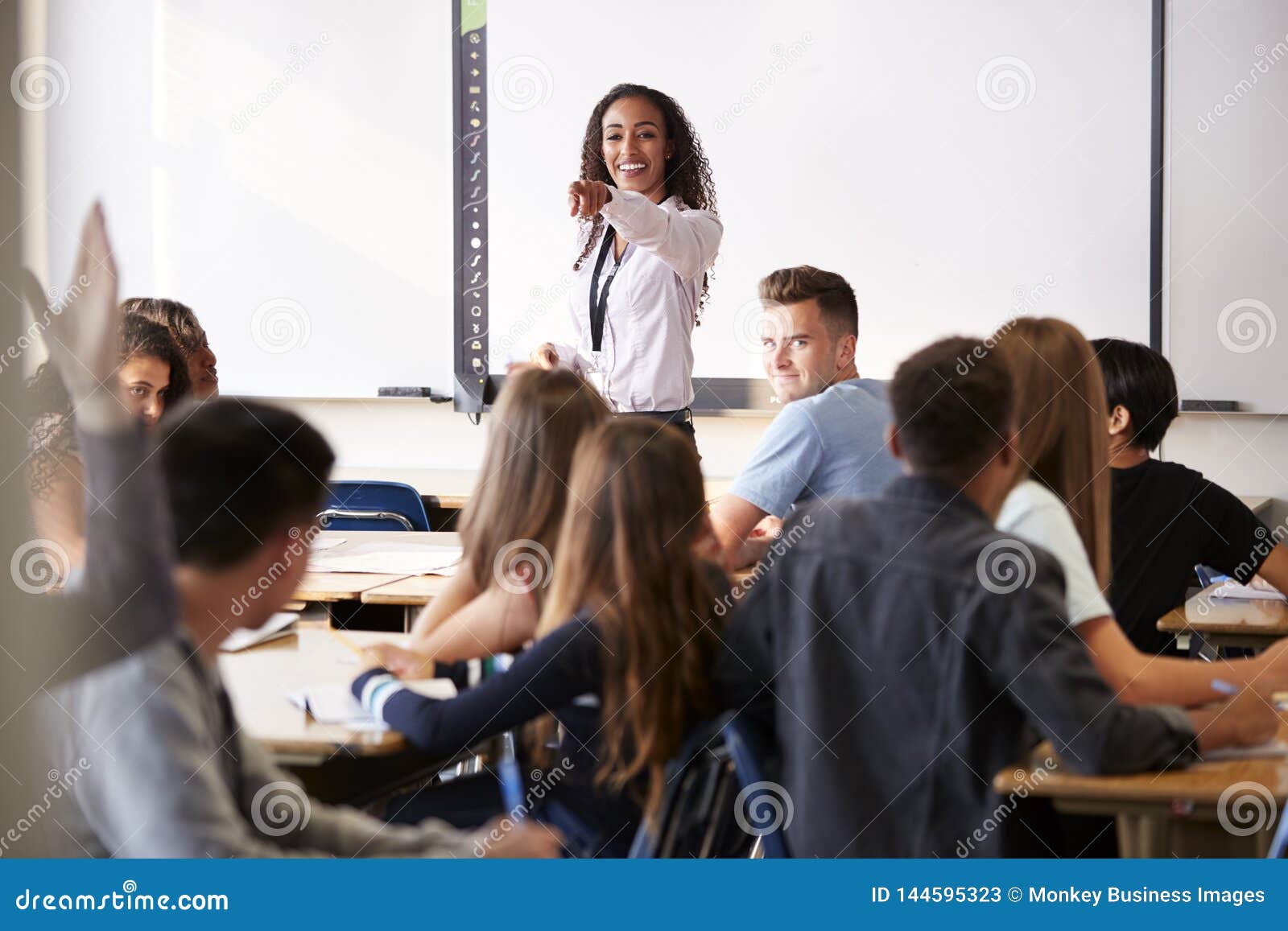 female high school teacher asking question standing by interactive whiteboard teaching lesson
