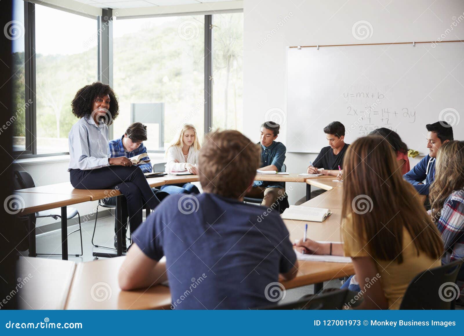 female high school tutor sitting at table with pupils teaching maths class