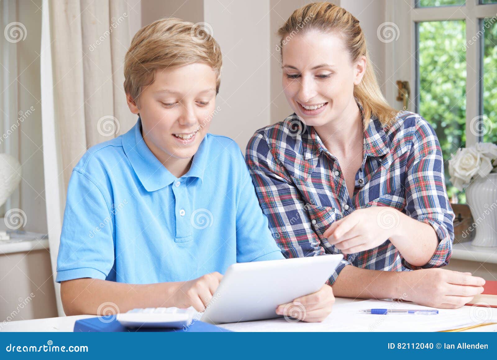 female home tutor helps boy with studies using digital tablet