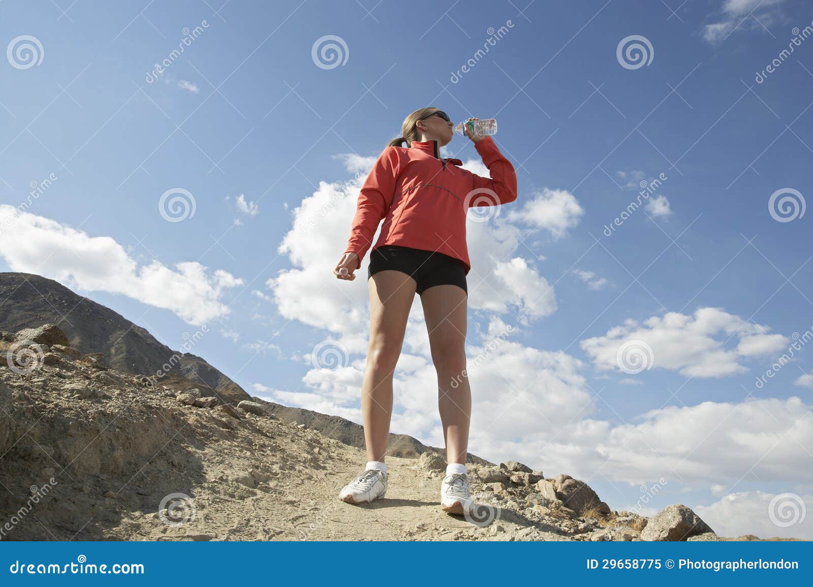 Female Jogger Drinking from Water Bottle in Mountains Stock Image