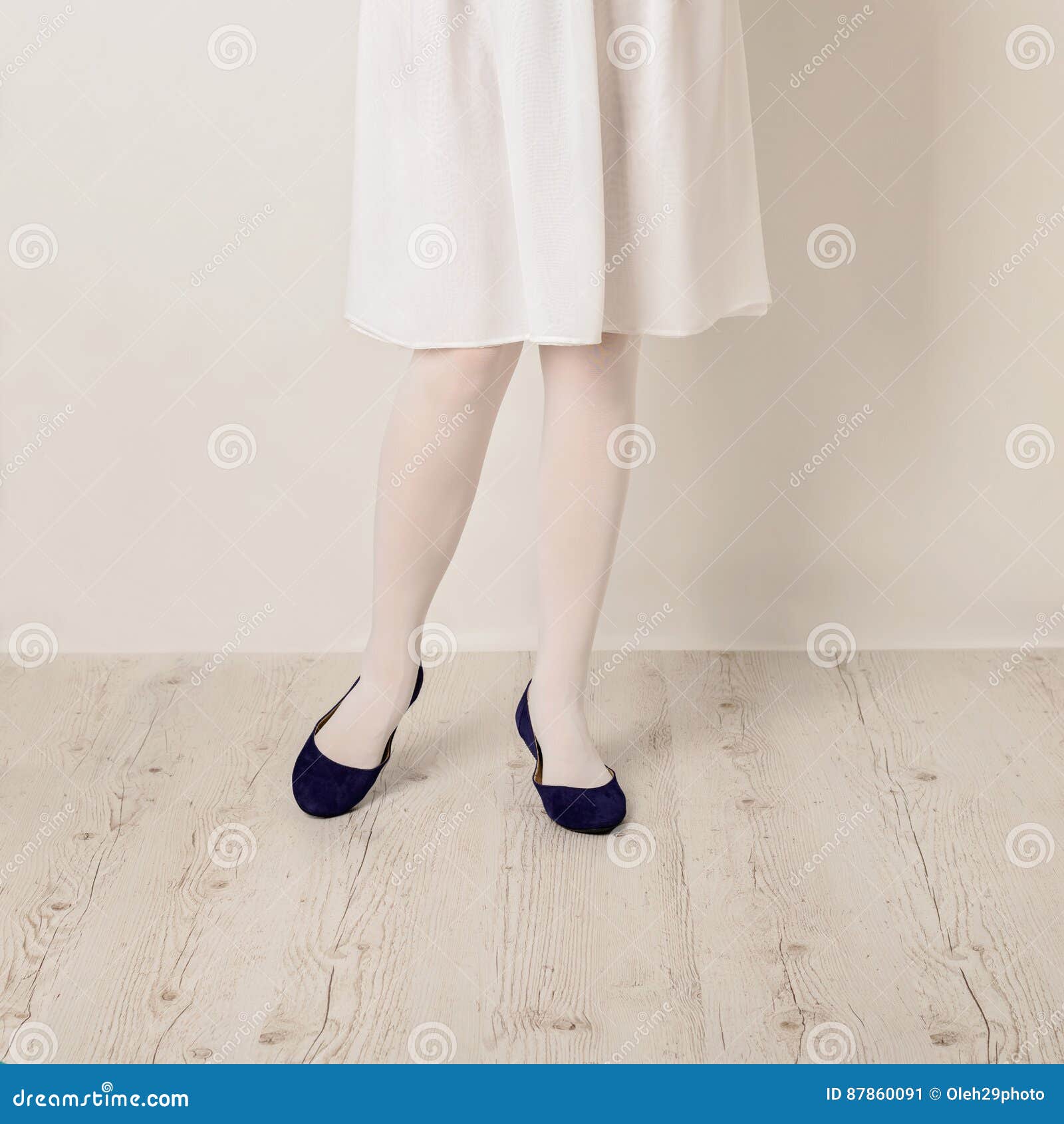 Female Legs in White Tights, Skirt and Ballet Flats on a White B