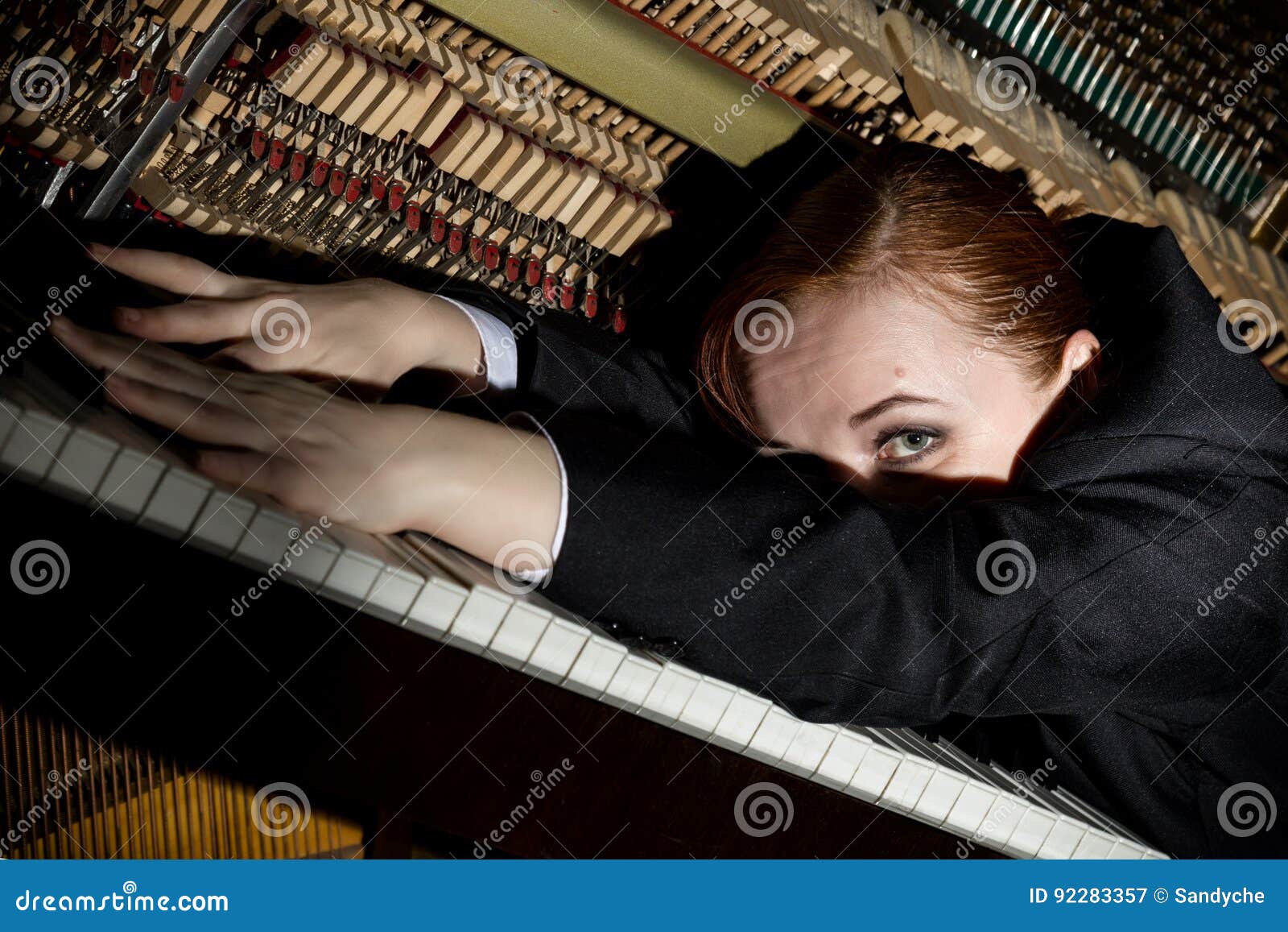 female musician dressed in a man`s suit lies on a piano keyboard