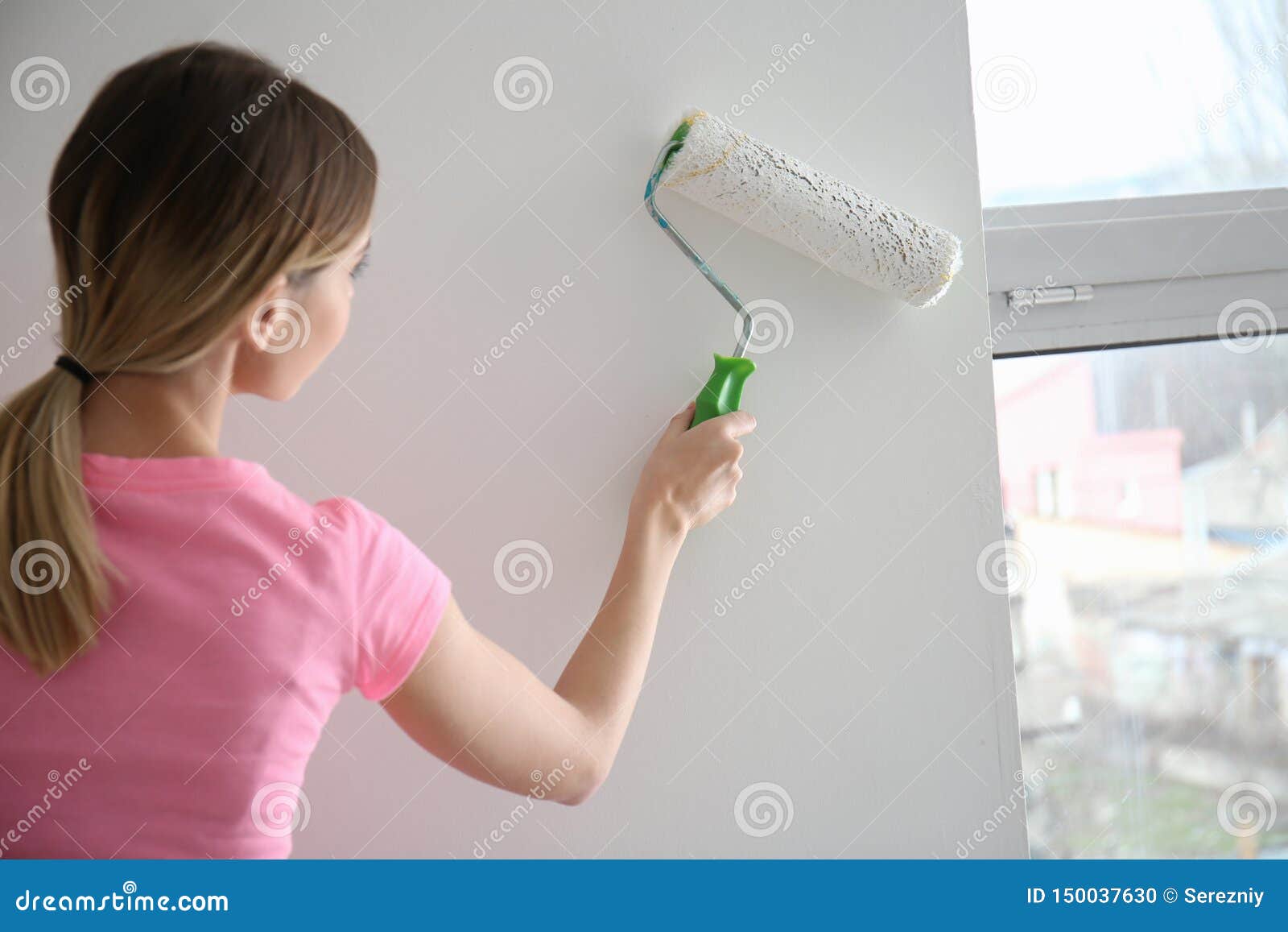 female painter using roller for refurbishing color of wall indoors