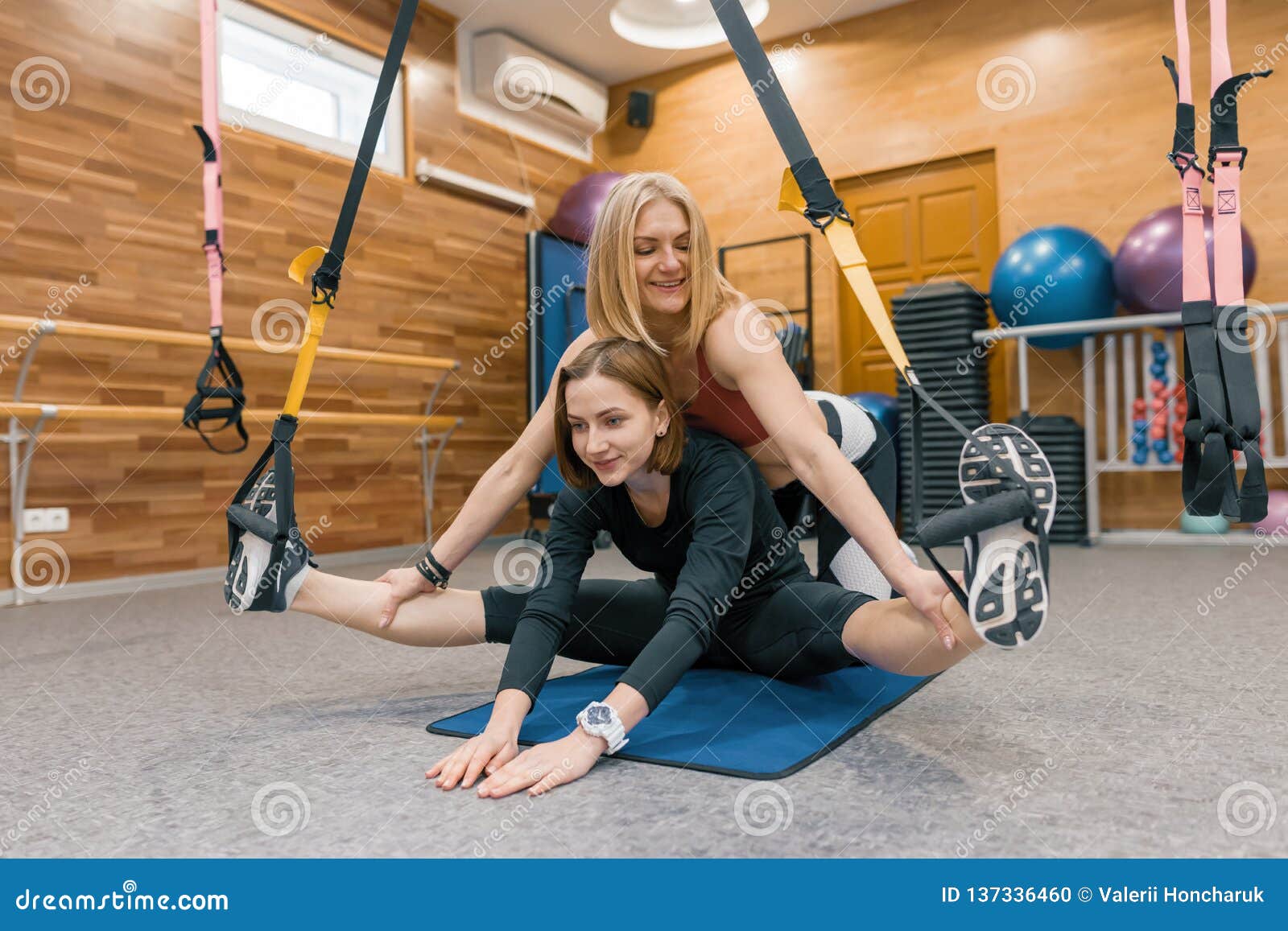 Female Personal Fitness Instructor Helping Young Girl To Do Exercis
