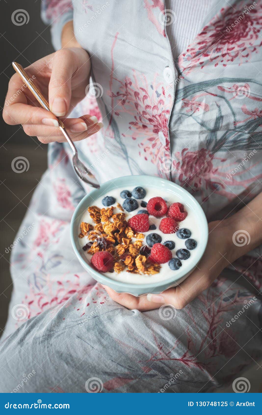 female in pijama eating yogurt with granola and berries