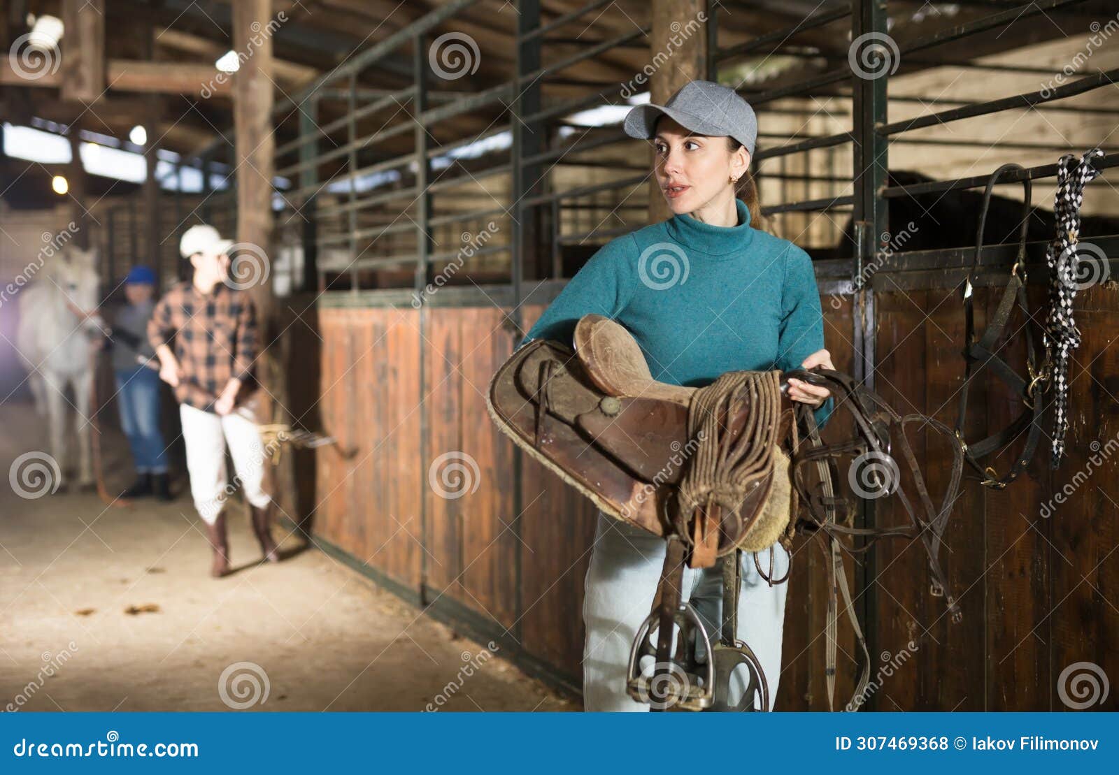 Female Rancher Carrying Horse Tack and Saddle in Horse Farm Stock Photo
