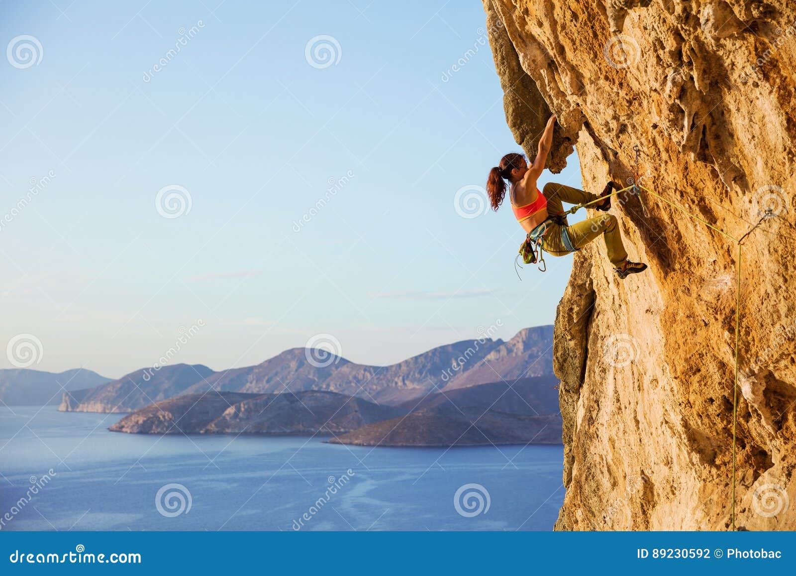 female rock climber on challenging route on cliff, view of coast