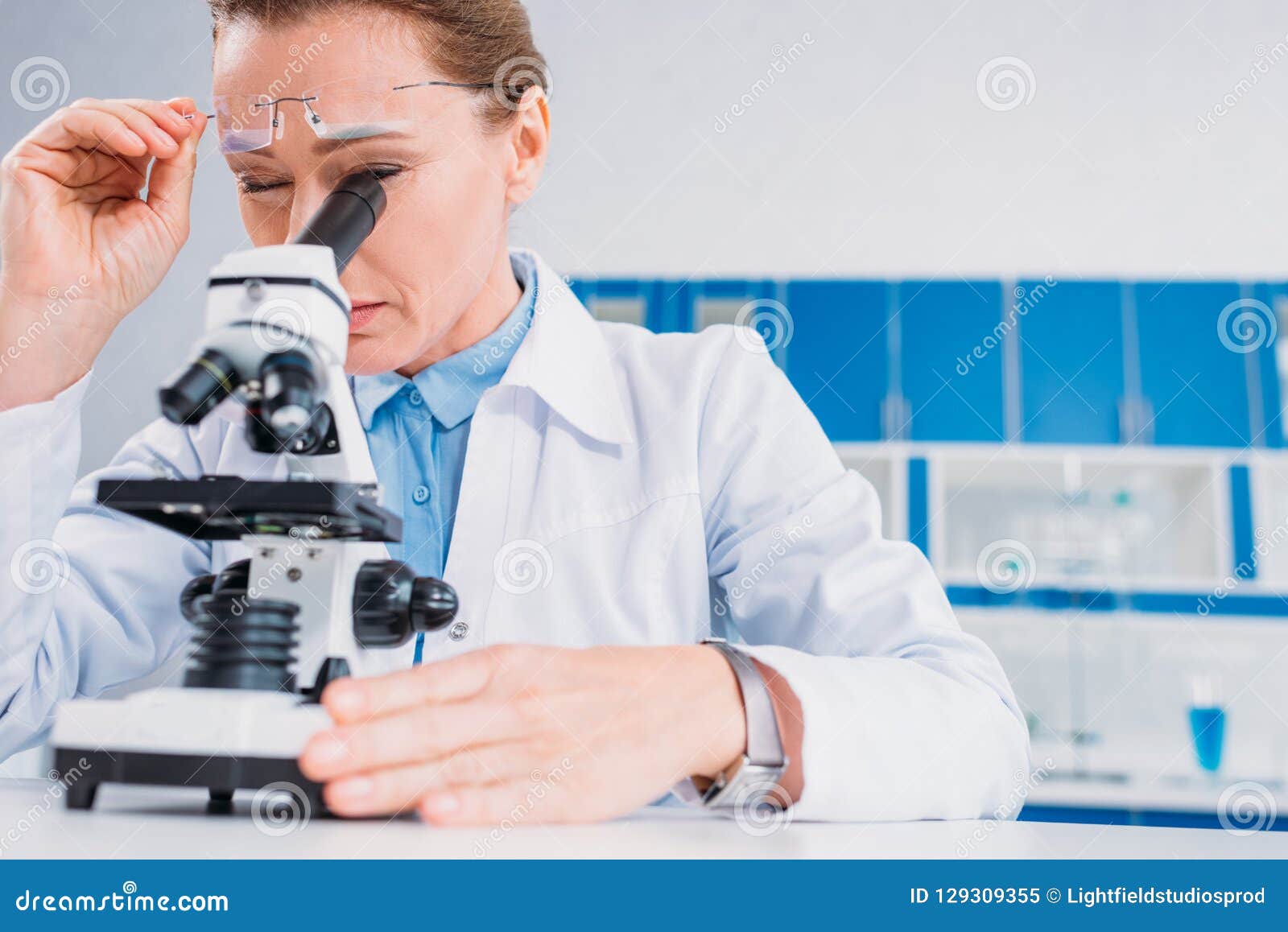 Female Scientist in Lab Coat and Eyeglasses Looking through Microscope