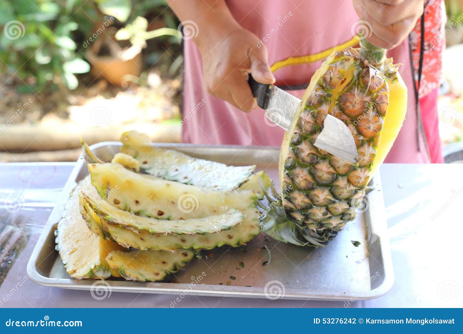 female seller's hands using a knife to pare pineapple