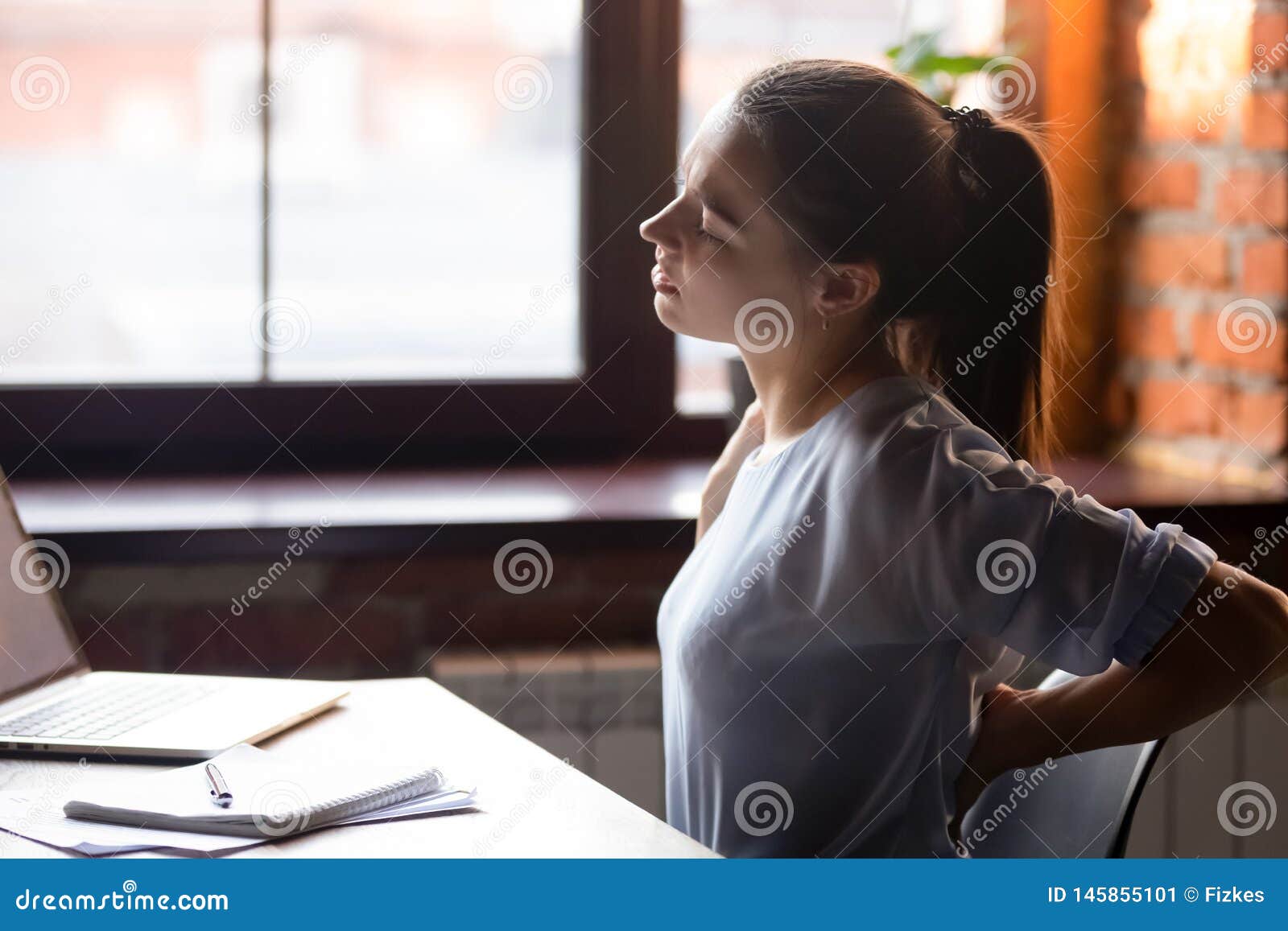 female sitting at table after sedentary work feels back ache