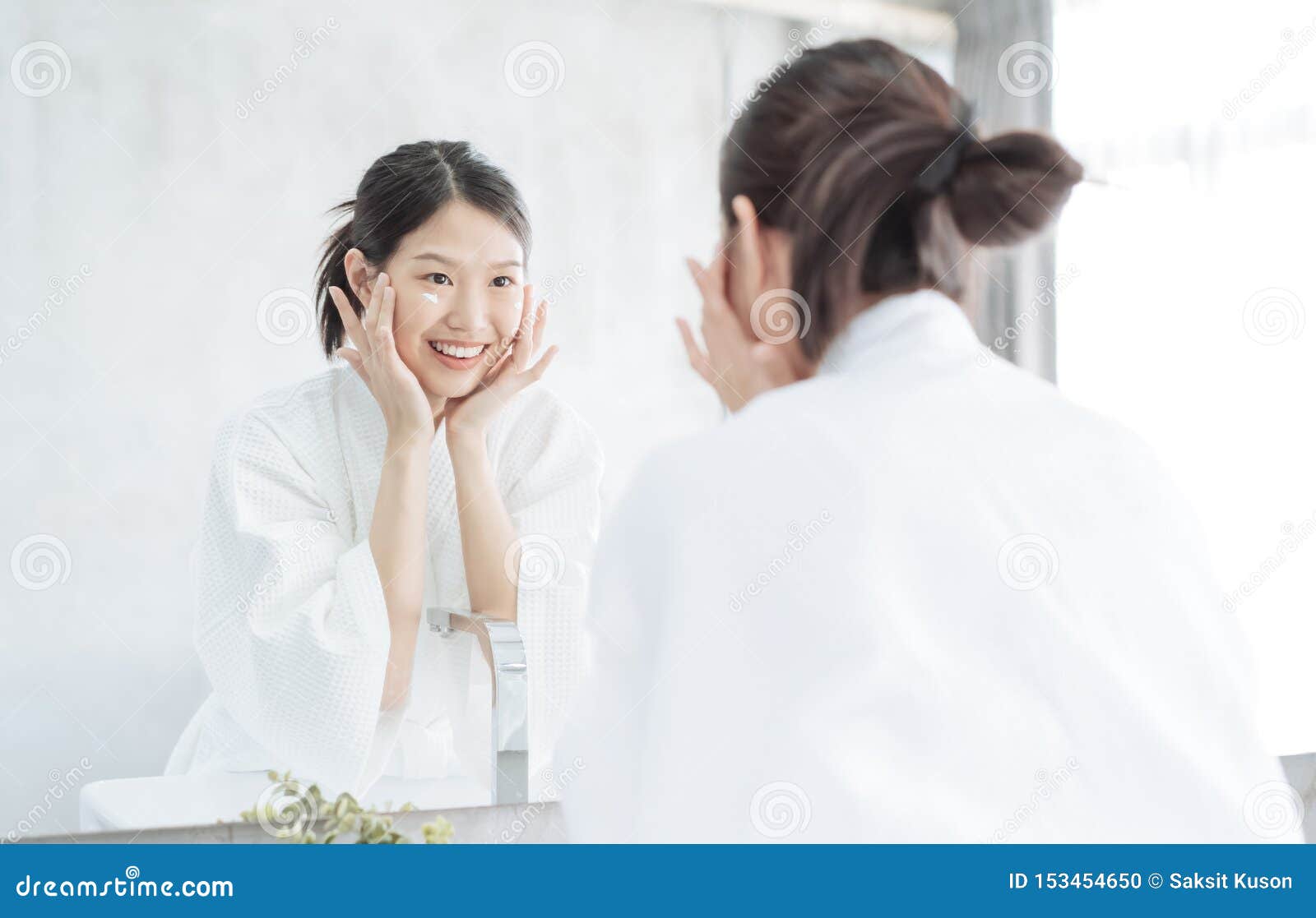 female skin care. young asian woman touching her face and looking to mirror in bathroom.