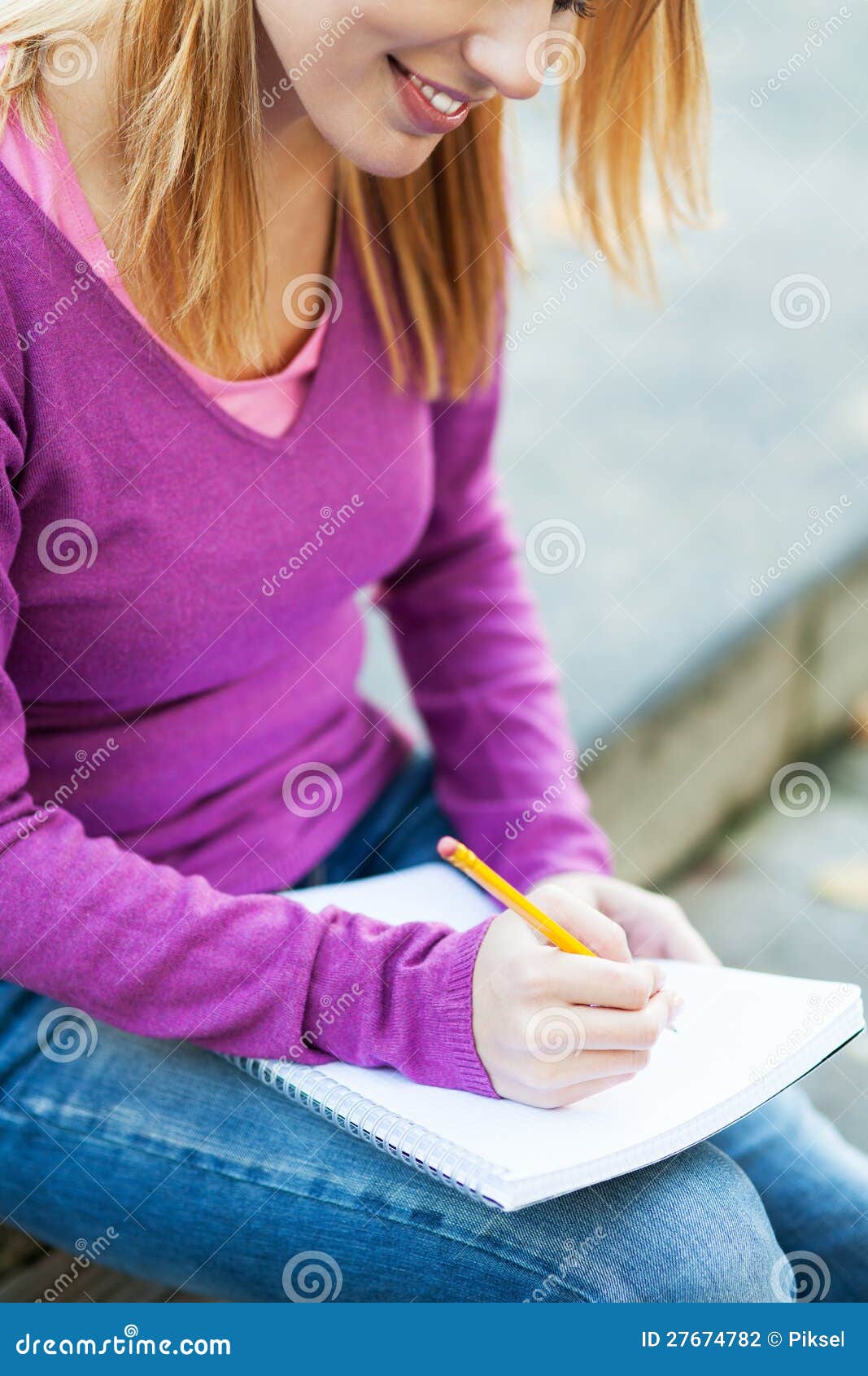 Female student writing in notebook. Portrait of a smiling woman outdoors